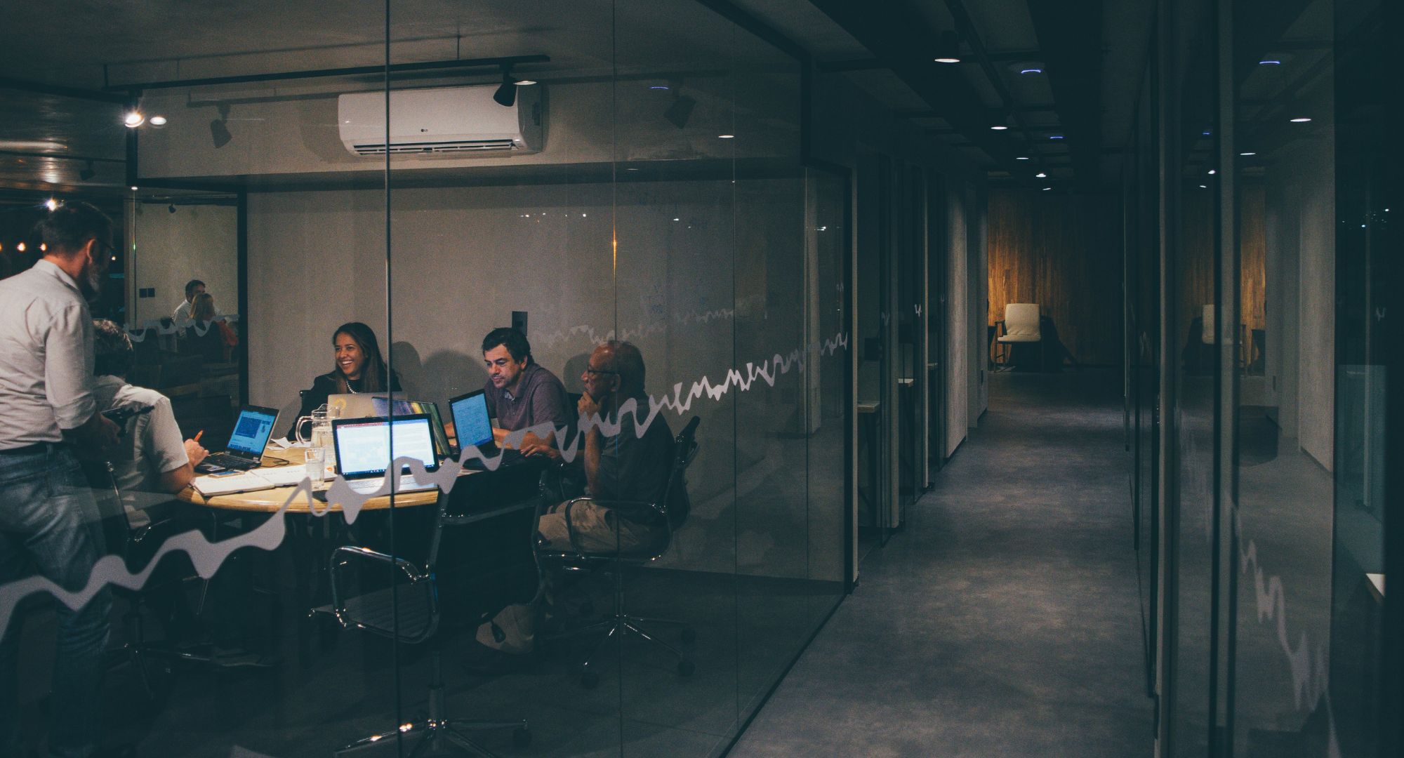 sala de escritório com vários notebooks e pessoas trabalhando