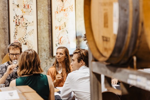 Groups enjoy a seated guided wine tasting in a barrel room with artwork in the background