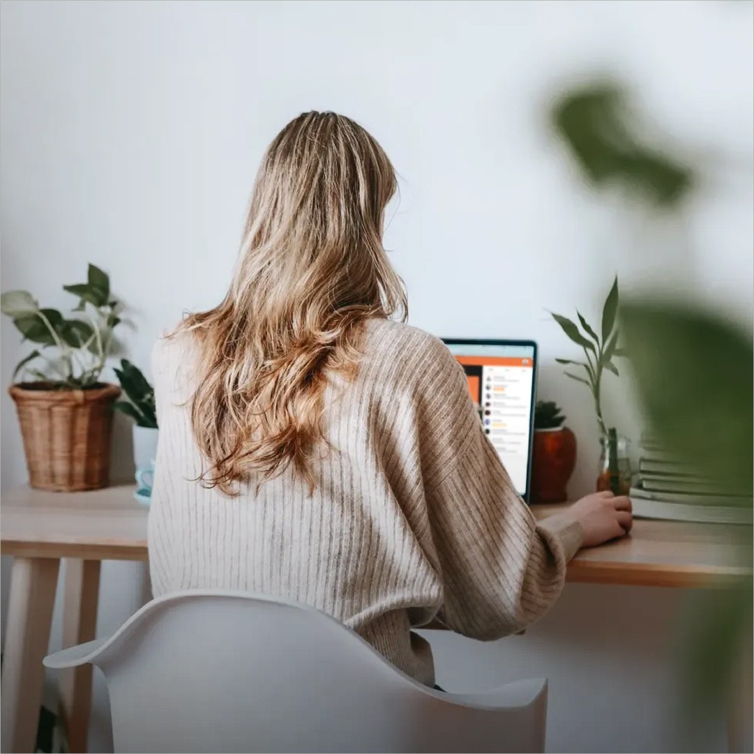Modern home office setup with a monitor, ergonomic chair, keyboard, and indoor plants near a window with blinds.