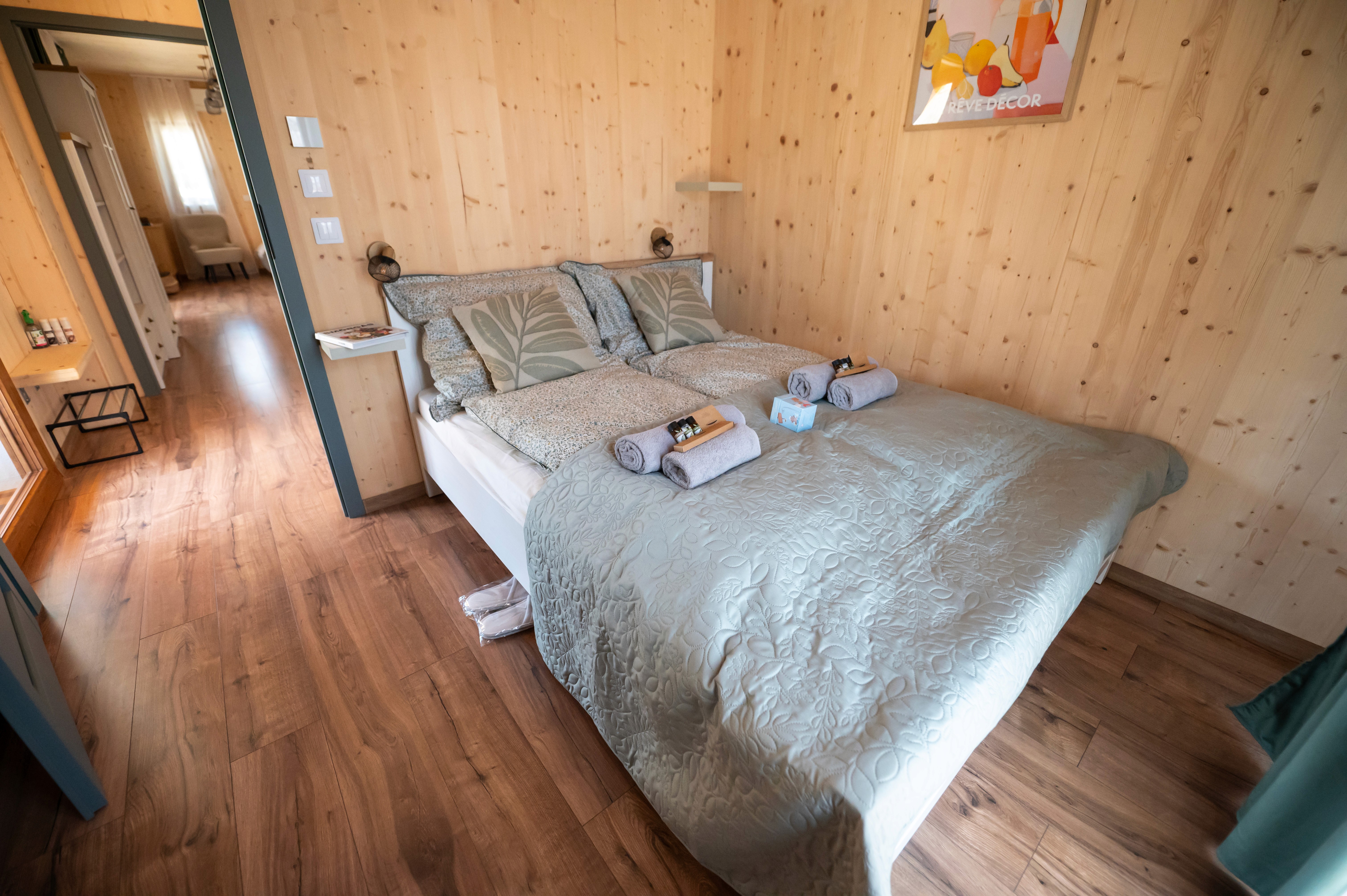 Hálószoba franciaággyal, modern szürke és zöld színű bevetett ágyneművel, rajta bekészített törölközők és kis ajándékok.