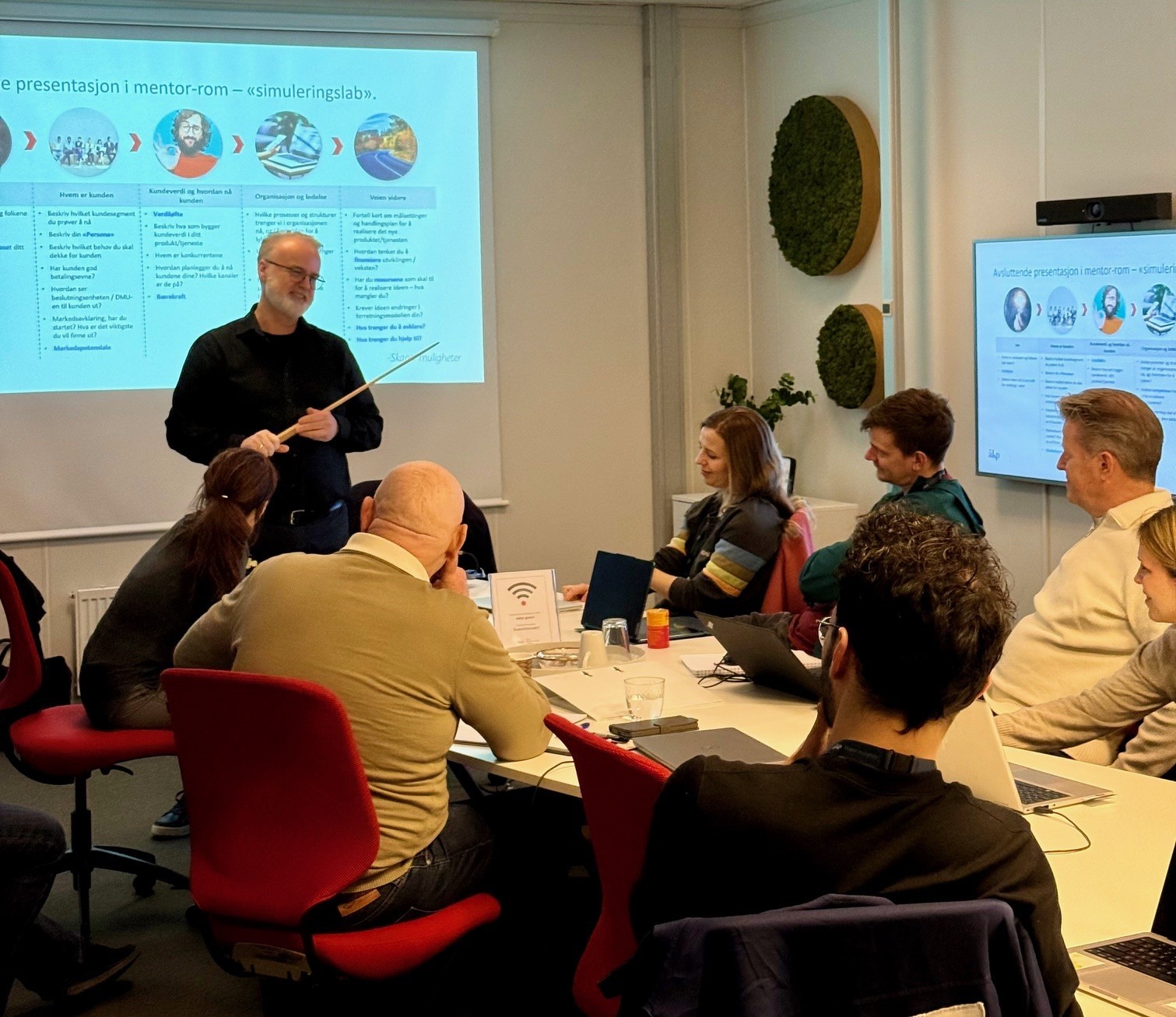 A person wearing a virtual reality headset stands in front of multiple screens, engaged in a digital experience.