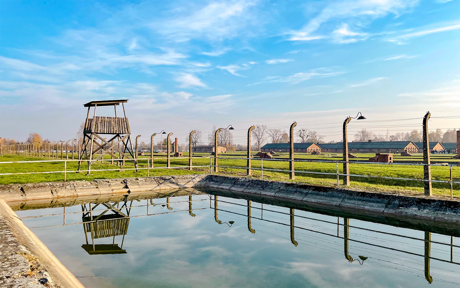Vagtårn og pigtrådshegn ved Auschwitz Birkenau, Polen, reflekterer i vandet.