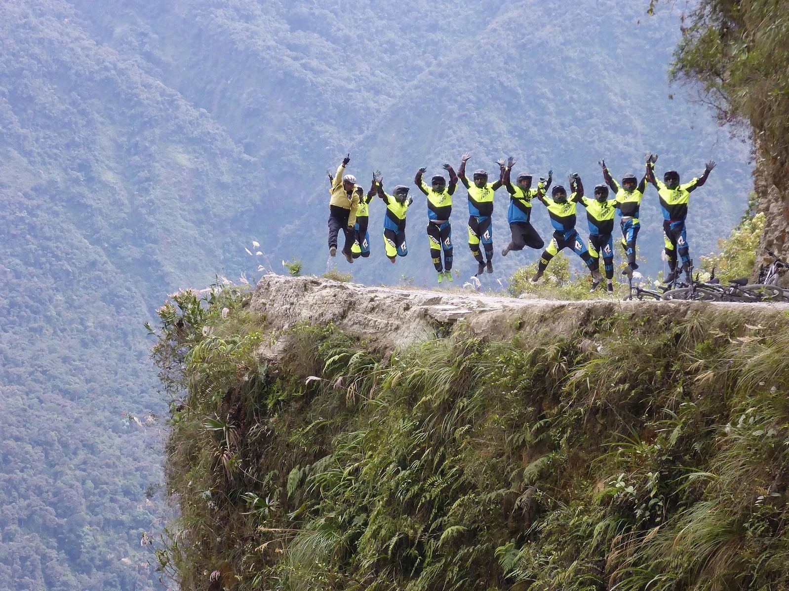 Group of bikers jumping on a cliffside dirt path.