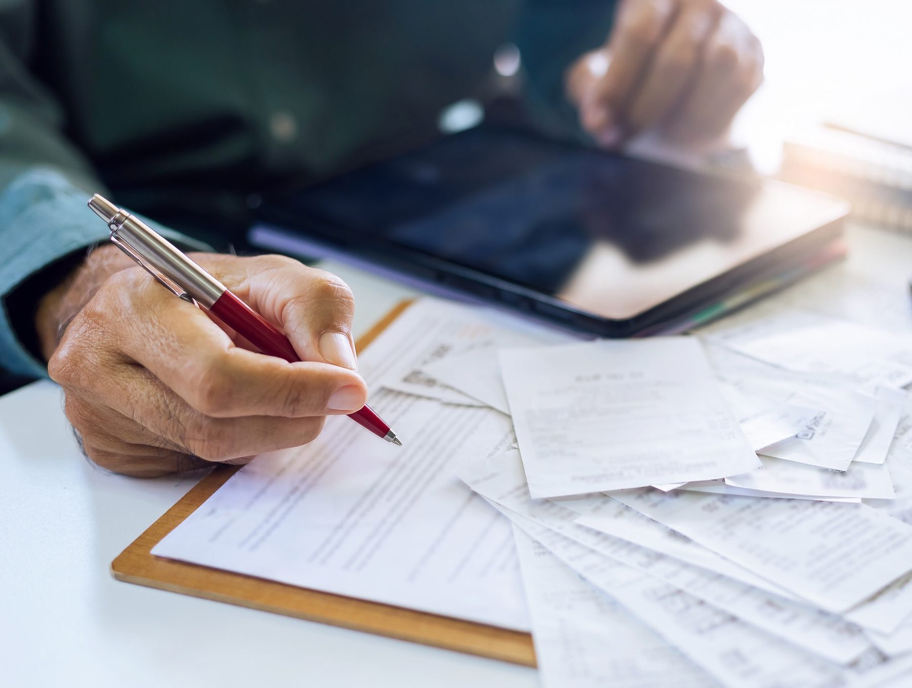 Person reviewing invoices and receipts alongside a tablet