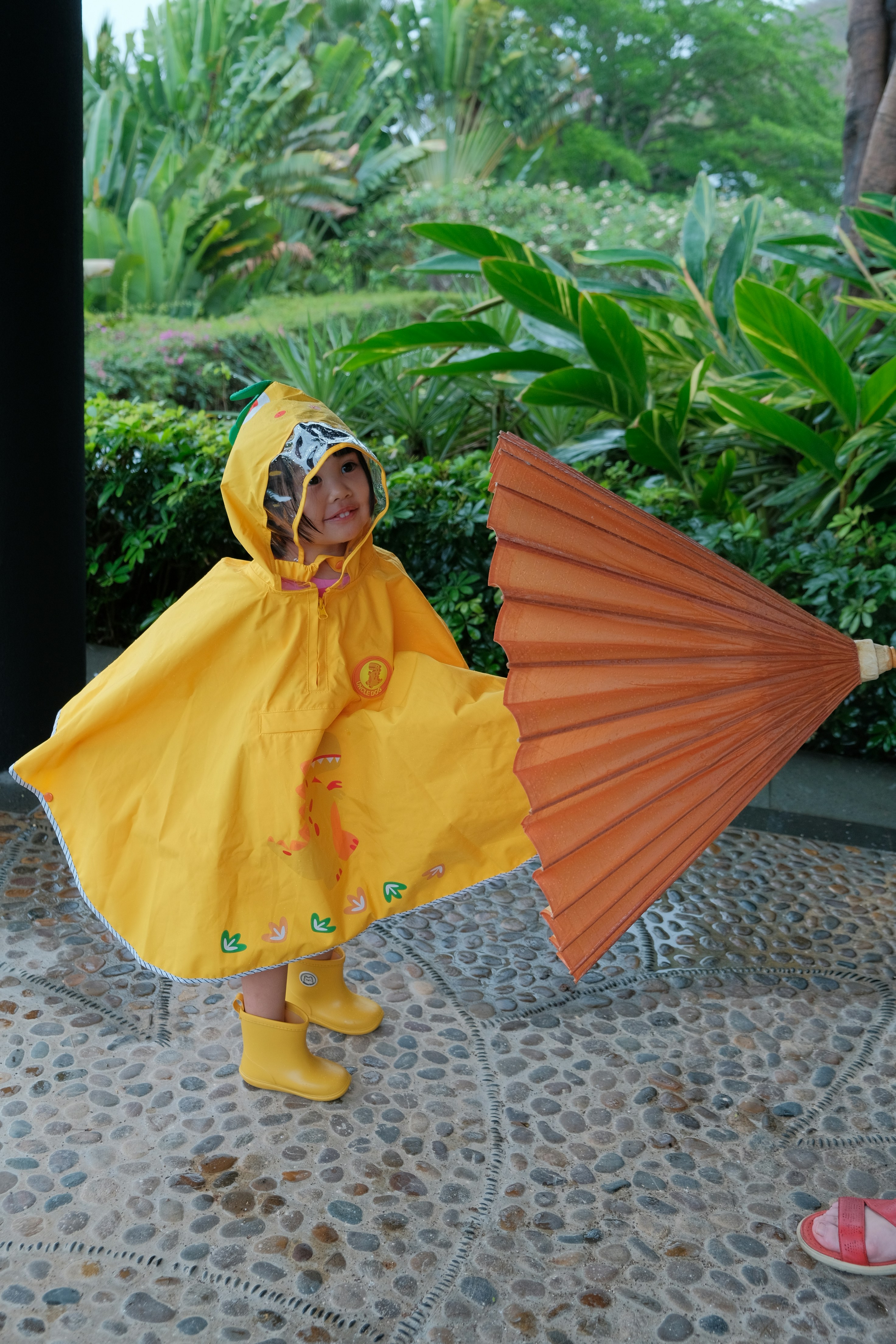 Young child in yellow raincoat holds large orange umbrella