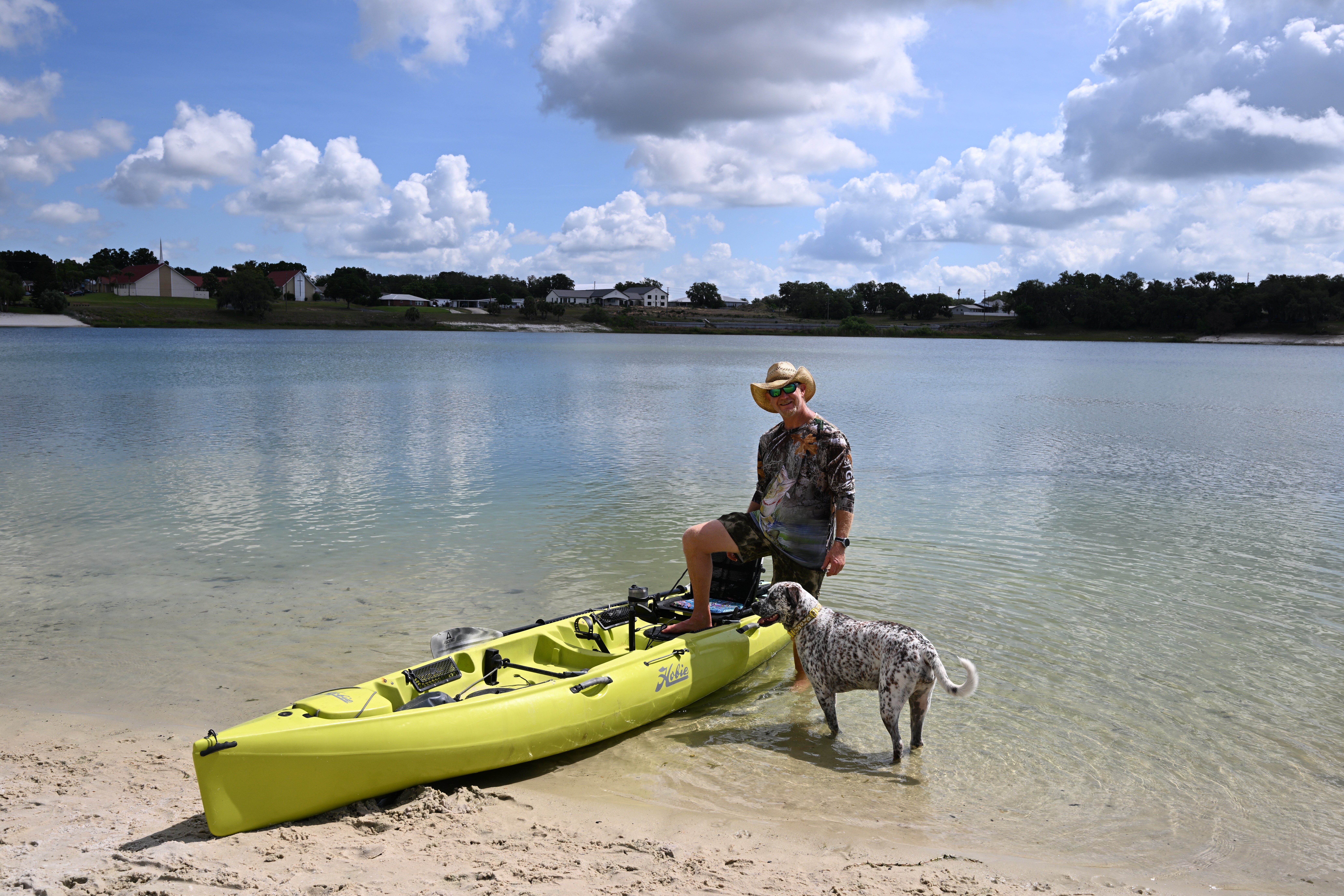 Man with a dog posing with a kayak on the bank of a lake