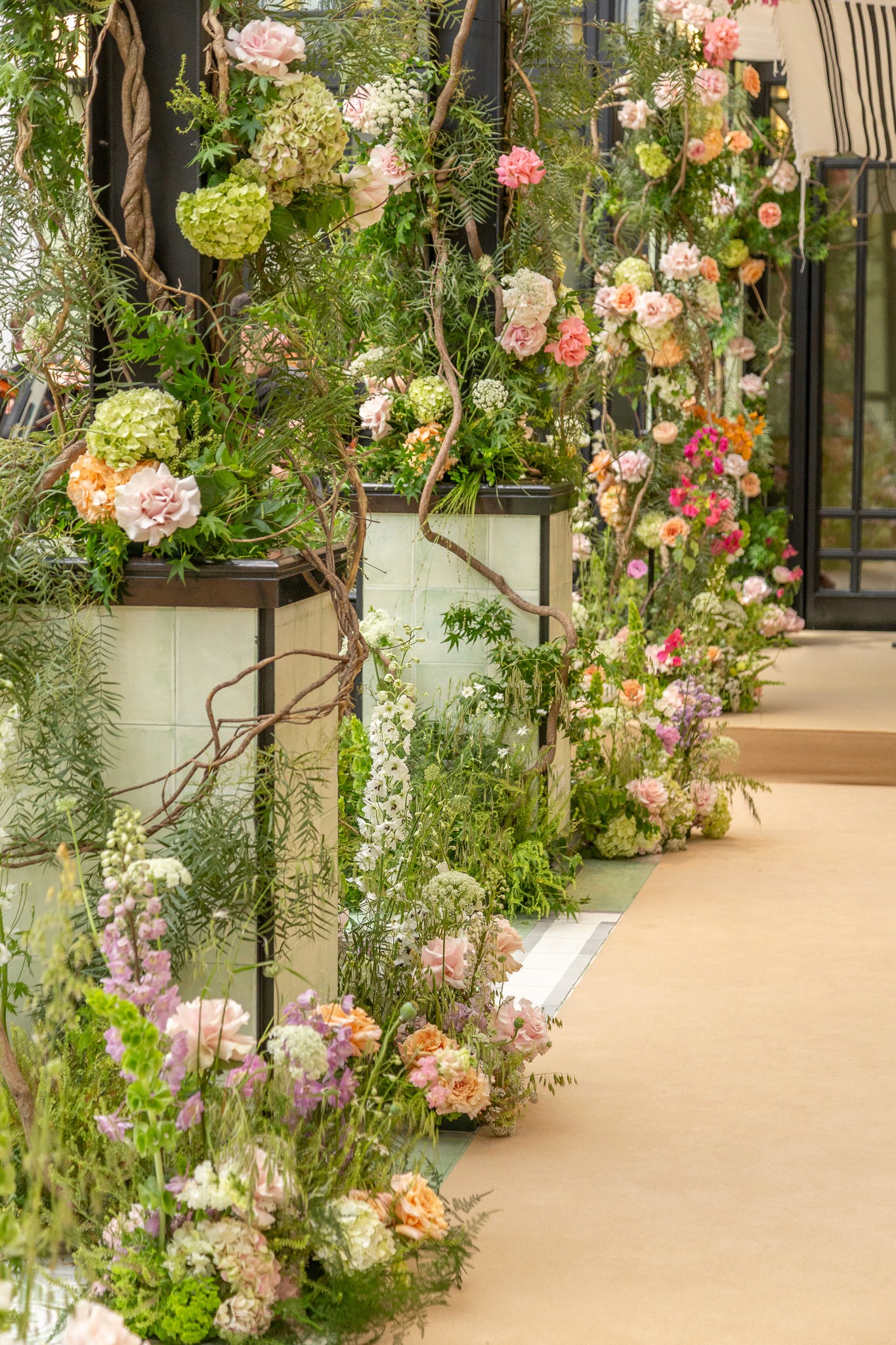 Pasillo de ceremonia en Alvear Icon con columnas de azulejos verdes y arreglos florales orgánicos en tonos pastel.