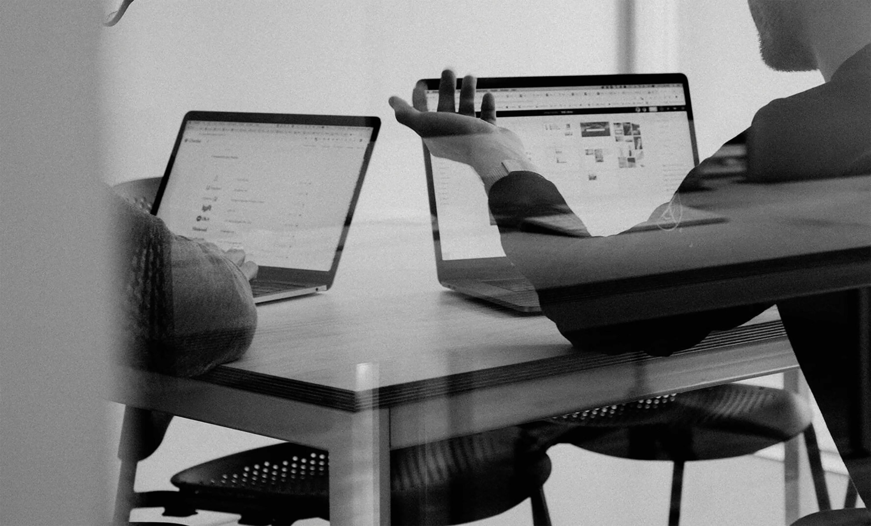 Black and white image of people working at a table with laptops, showing hands gesturing during discussion of digital content displayed on screens, with fabrica® logo in the corner.