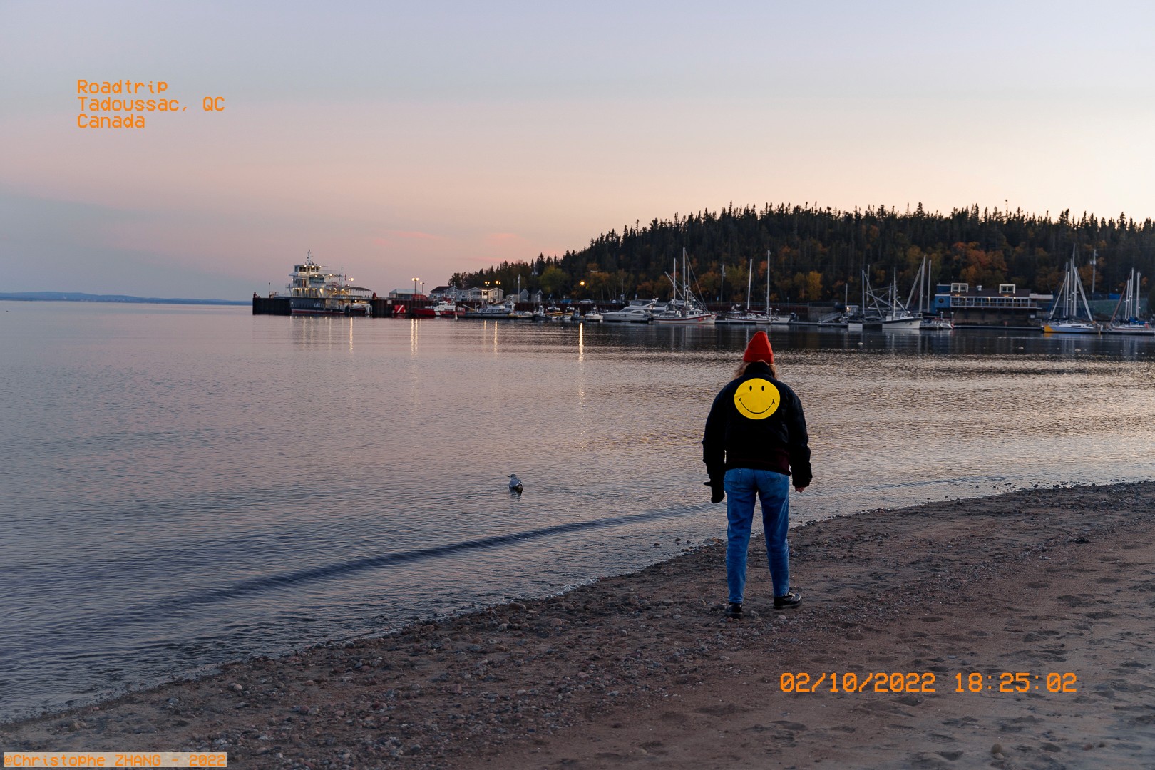  Personne en bord de mer à Tadoussac au crépuscule, avec un ferry et des voiliers à l'horizon.