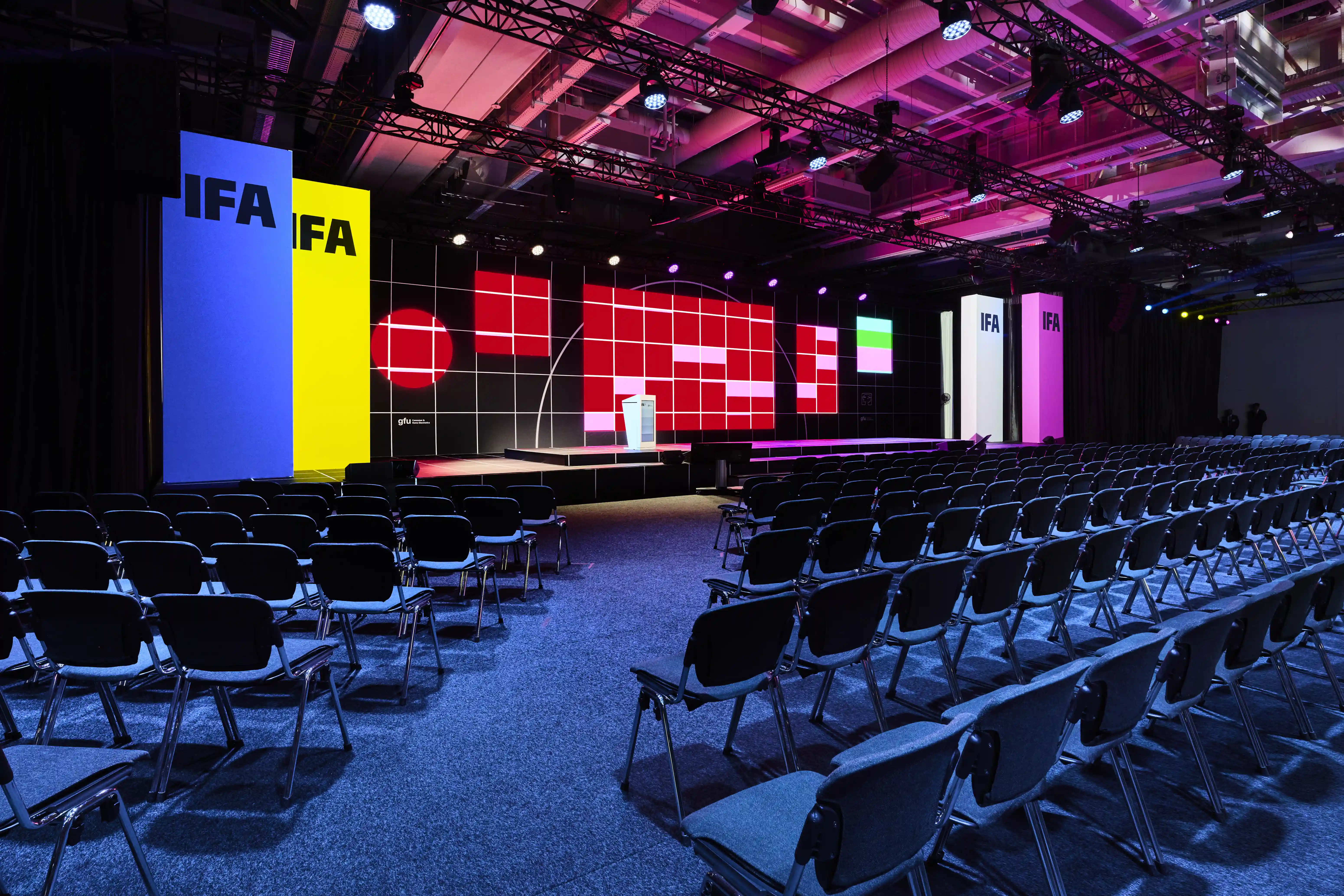 IFA keynote stage with colourful LED grid wall, lectern and rows of chairs in pink light.
