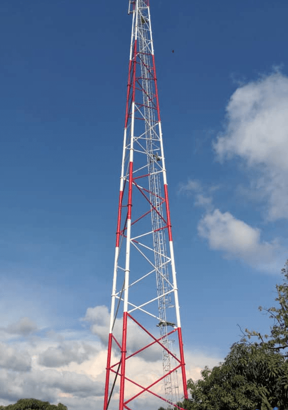 A smiling young man with crossed arms, wearing a plaid shirt and white t-shirt, poses against a dark background.