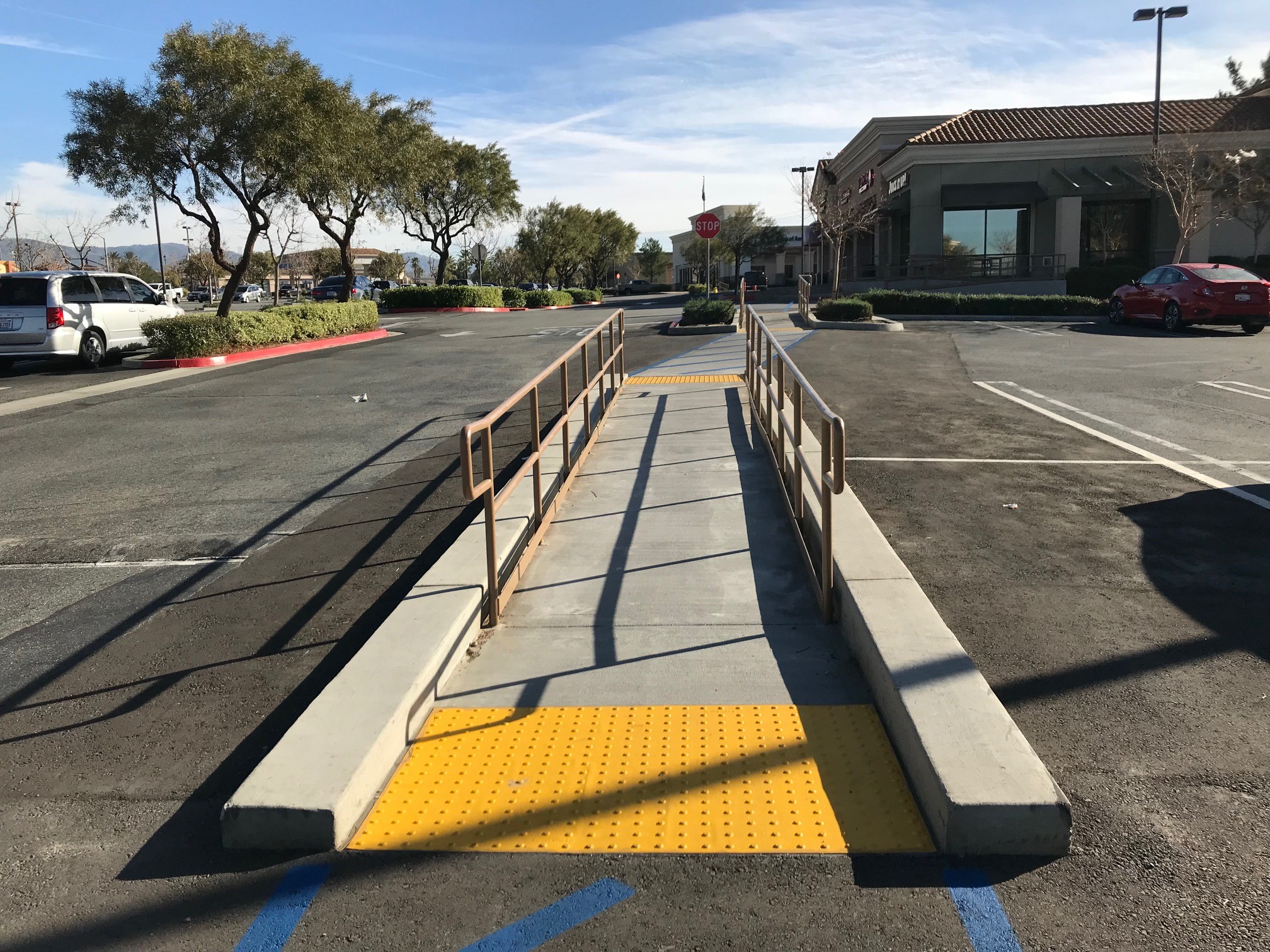 concrete sidewalk, curb, truncated domes, and handrail