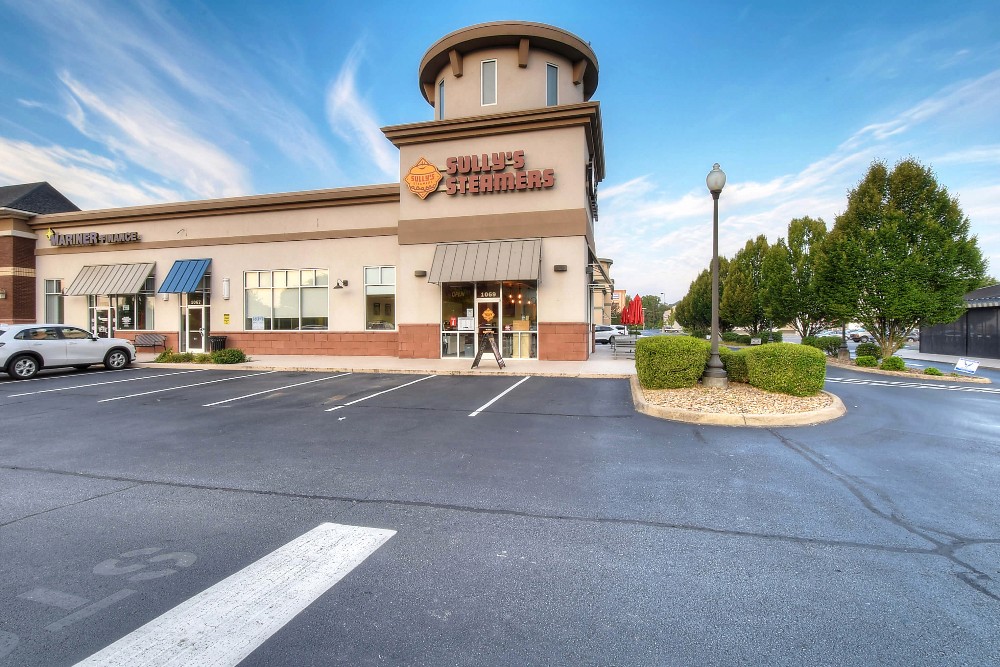 A wide shot of a building with a tower, set against a clear blue sky and surrounded by parking spaces.