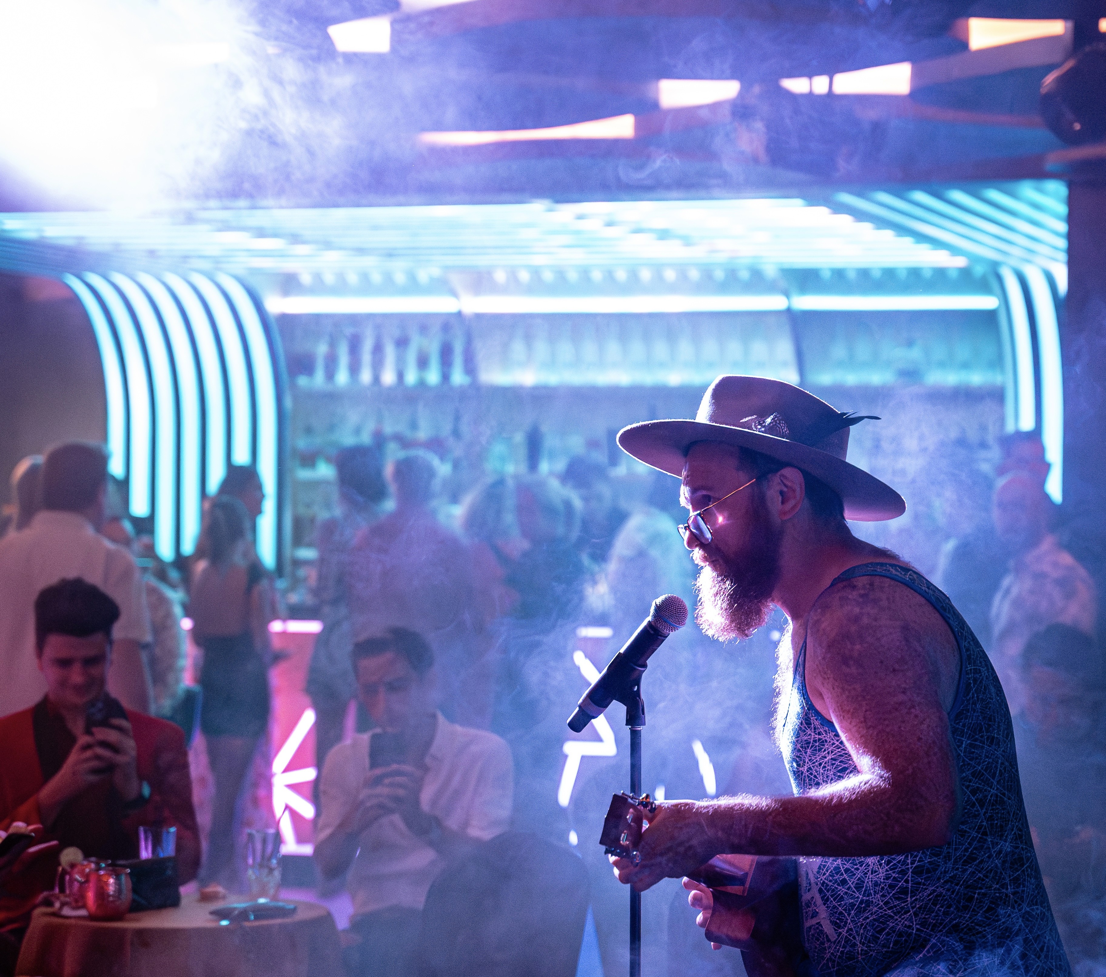 Atmospheric event photography of a live singer under blue and pink neon lights, capturing the high-energy crowd at the venue.