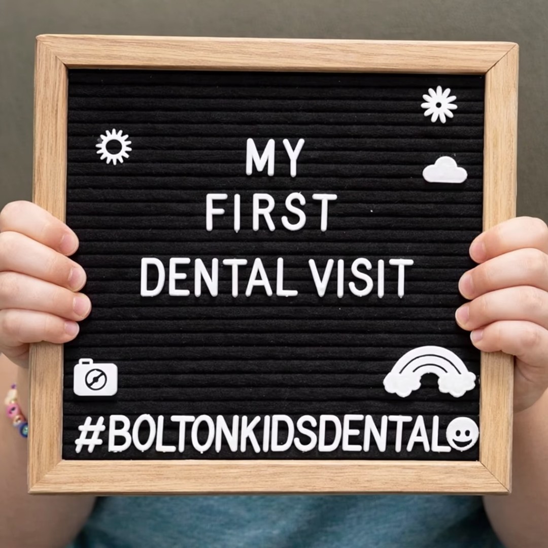 A child holding a black letter board that reads "My First Dental Visit #BoltonKidsDental" with sun and rainbow icons.