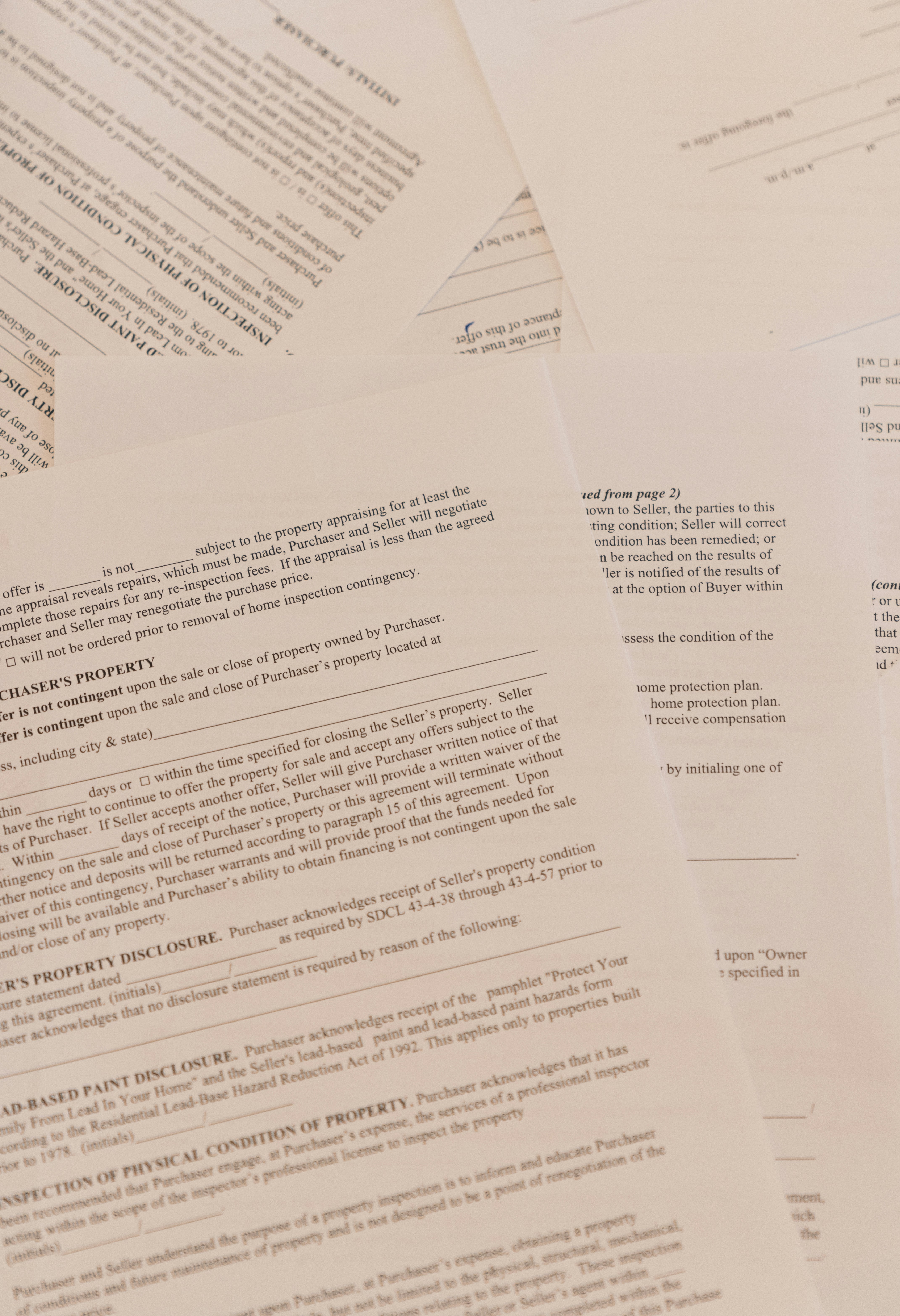 Stack of legal contracts and disclosure documents spread across a desk, showing dense fine print and signature lines on multiple pages.