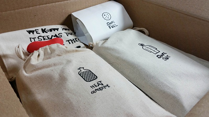 A photo of two textile bags and some pieces of paper in a card box. The bags seem to contain a heat gatherer and a raincoat.