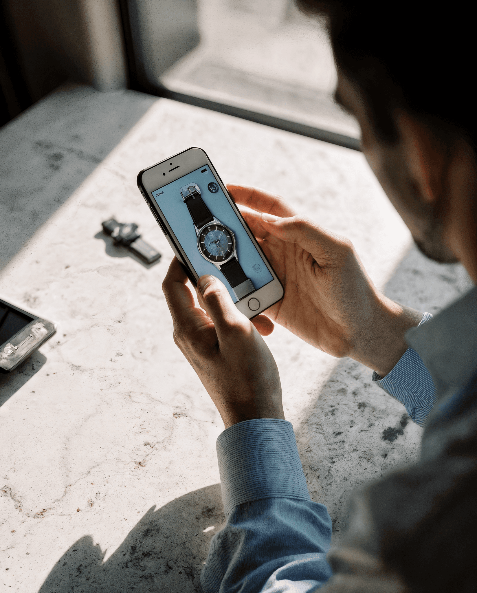 Man in glasses using phone at desk with laptop.