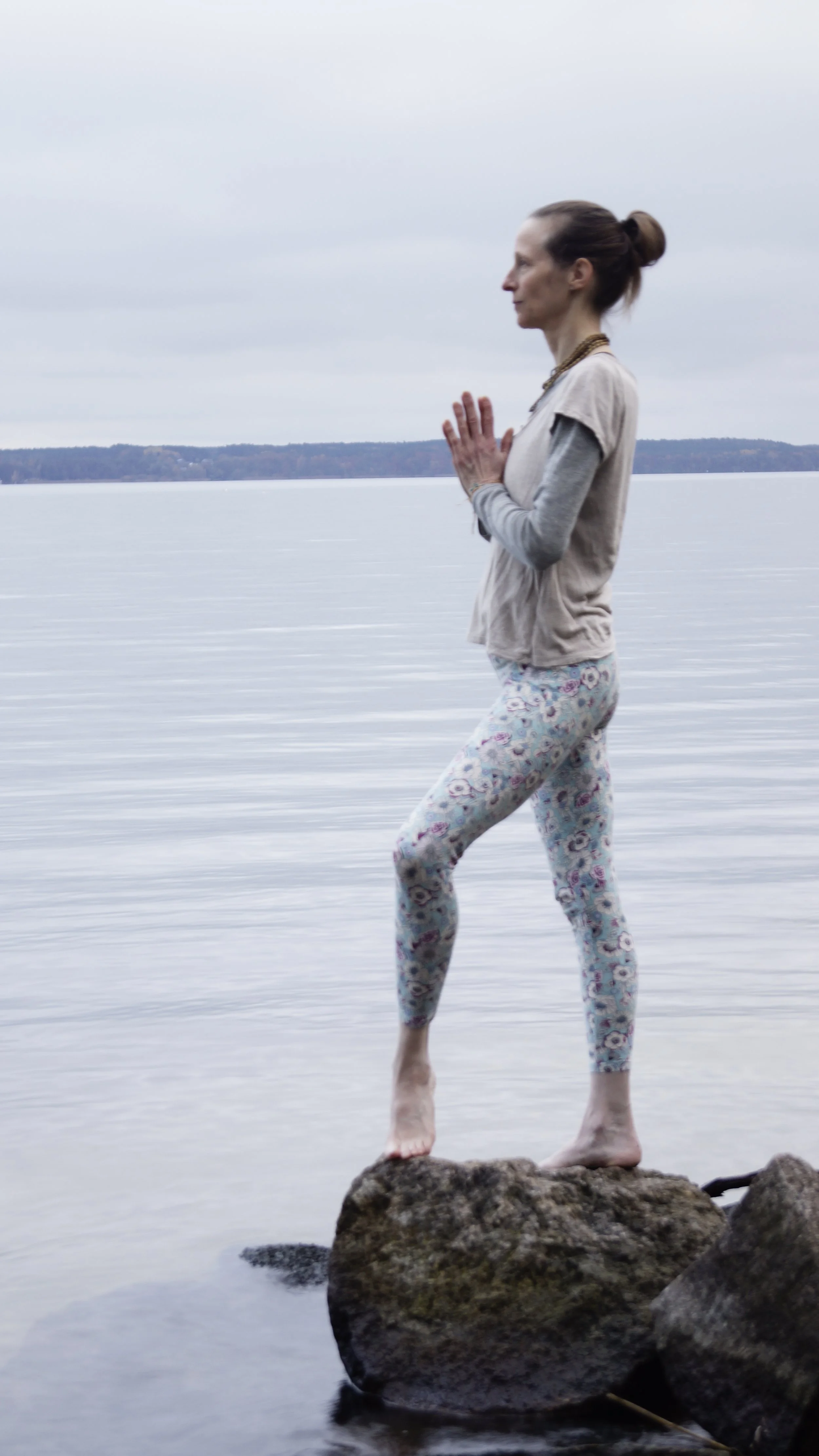 Karina Gaurangi Schmuck ist aufrecht stehend auf einem Stein, mit dem linken Bein einen kleinen Schritt nach vorne (Bein ist leicht gebeugt) und Anjali Mudra (Handflächen aneinander gelegt) vor dem Herzen