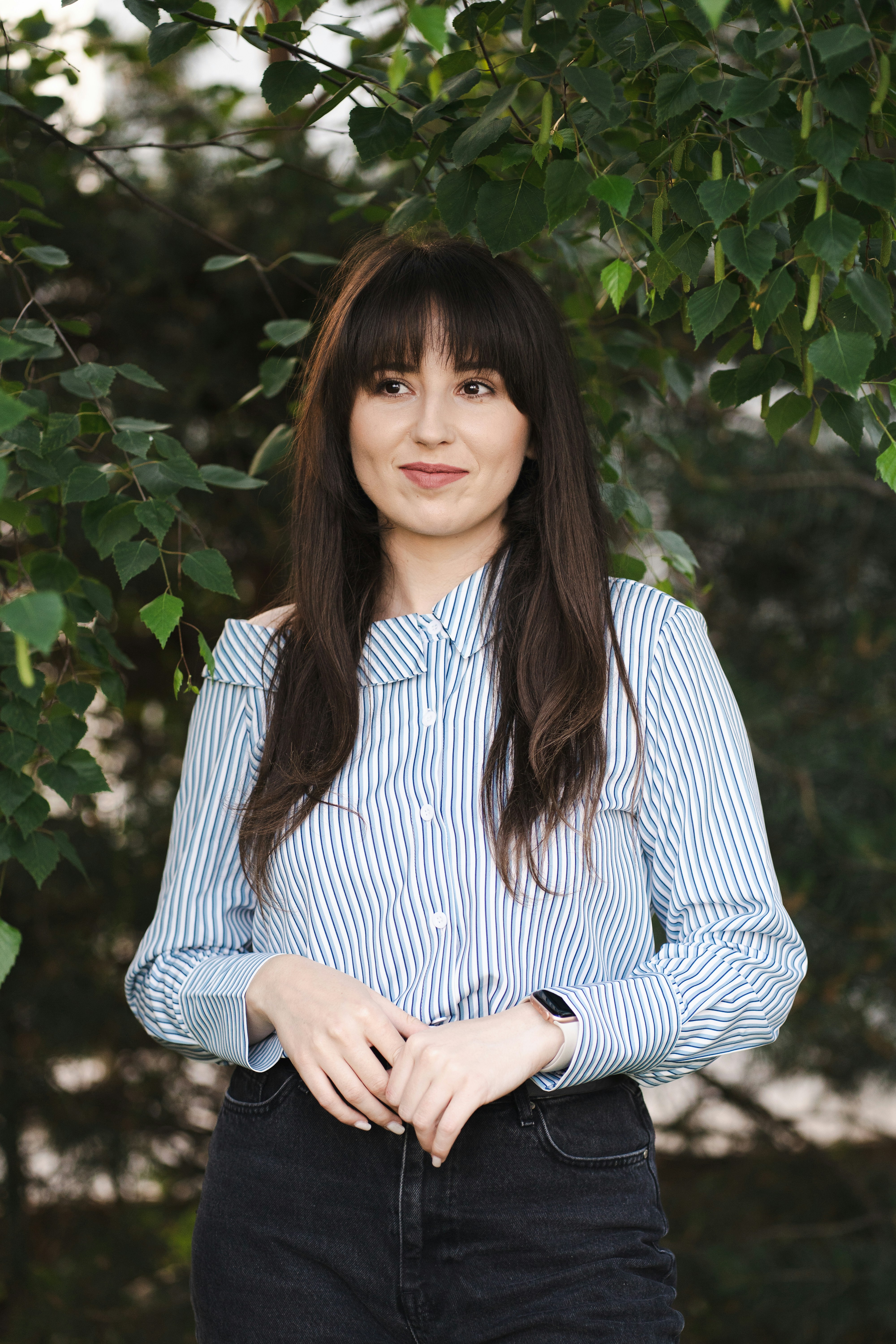 Woman smiles while posing near foliage.
