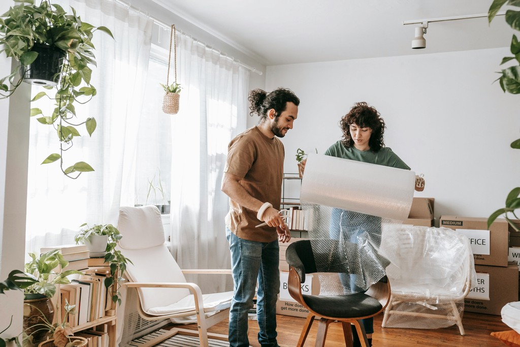 Two people assembling furniture in a bright living room with packed boxes
