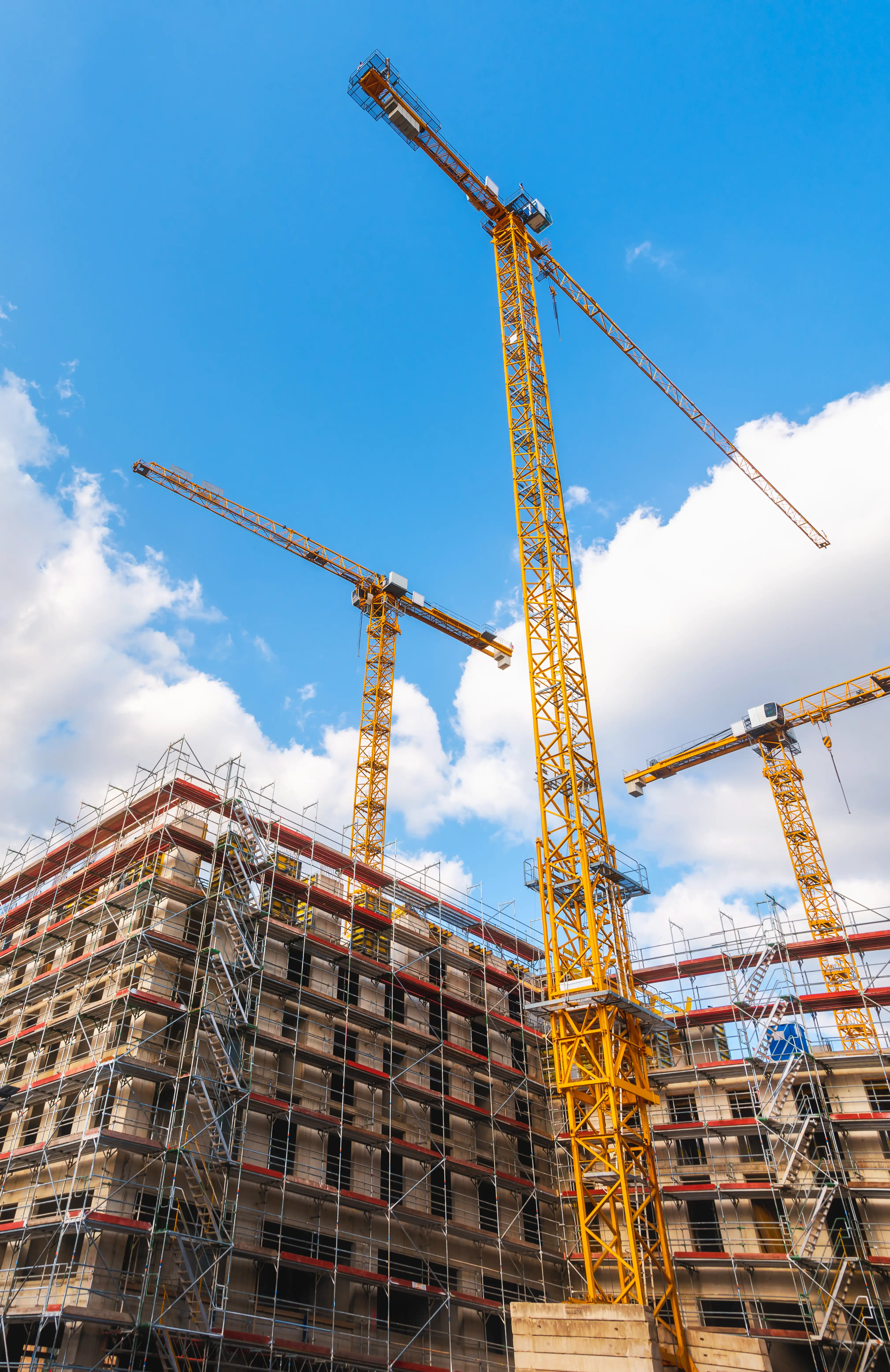Yellow construction cranes standing tall against a bright blue sky with white clouds.
