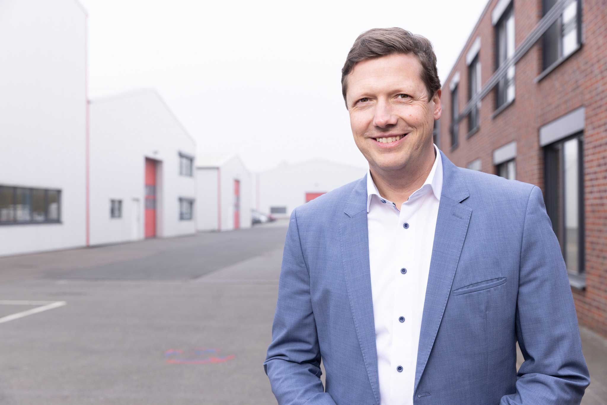 Portrait eines lächelnden Mannes im blauen Sakko vor Industriekulisse. Manager, Geschäftsführer.