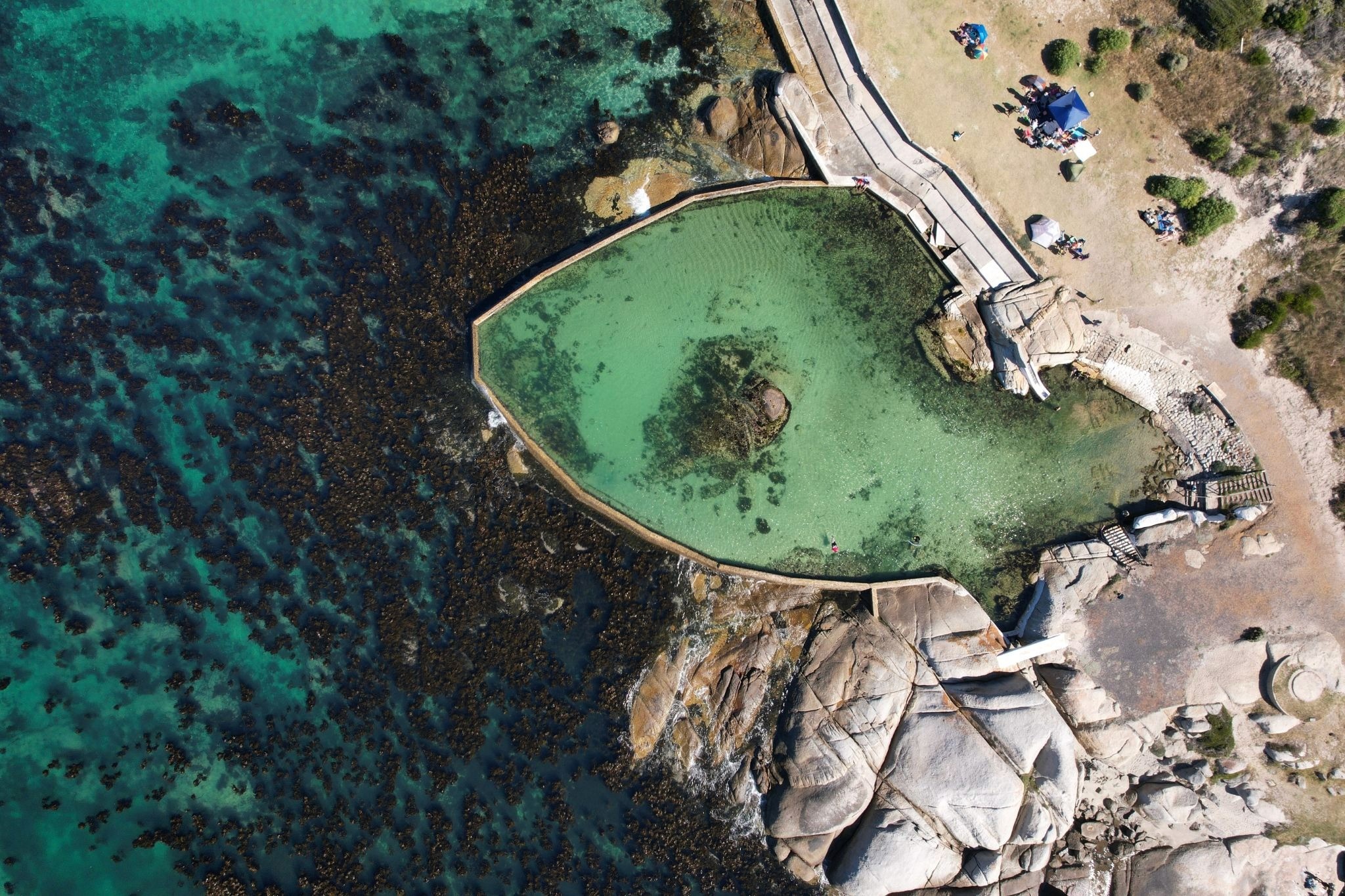 Overhead shot of a turquoise pool with rocks in it and the sea on the left