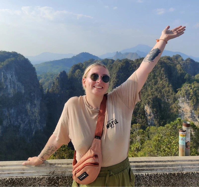 Jade on top of a mountain with one arm up
