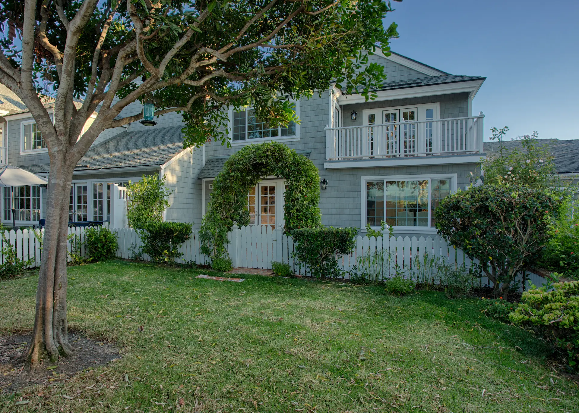 Charming Cape Cod style home featuring a lush green lawn and a classic white picket fence. Part of the Dana Point Cape Cod remodel. Photo by Chris Darnall.