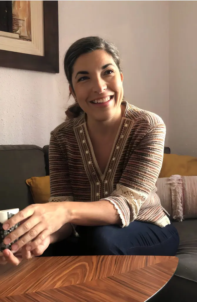 Headshot of Virginia Vila smiling, seated on a sofa in a relax indoor setting