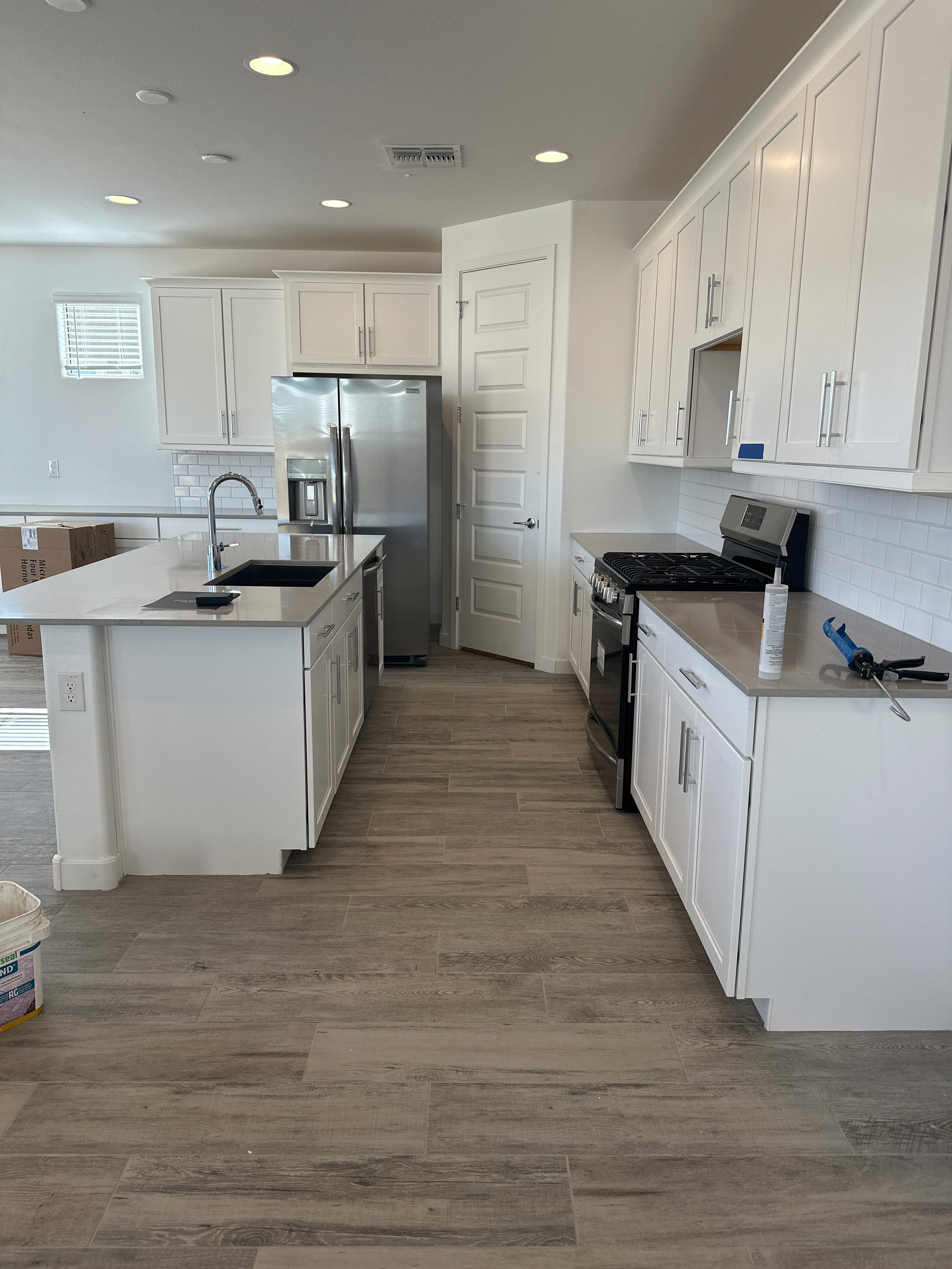 Modern kitchen with white cabinets, stainless steel appliances, granite countertops, and wood-look tiles.
