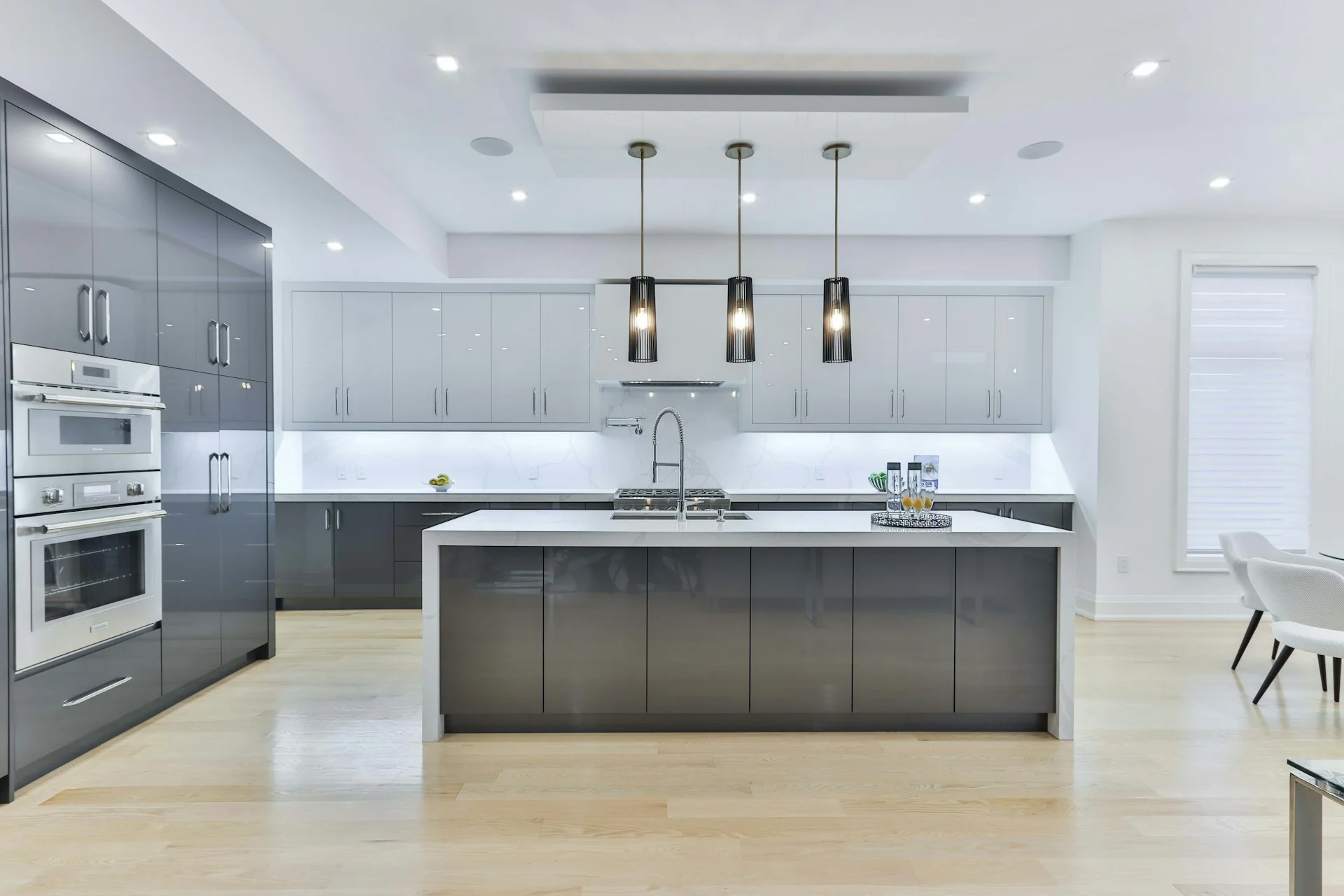 Bright contemporary kitchen with a large island, glossy cabinets, pendant lights, and a minimalist white design.
