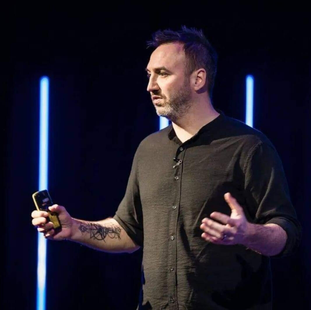 Phil Quirk addressing an audience, explaining concepts of NLP with engaging gestures and a confident demeanor.