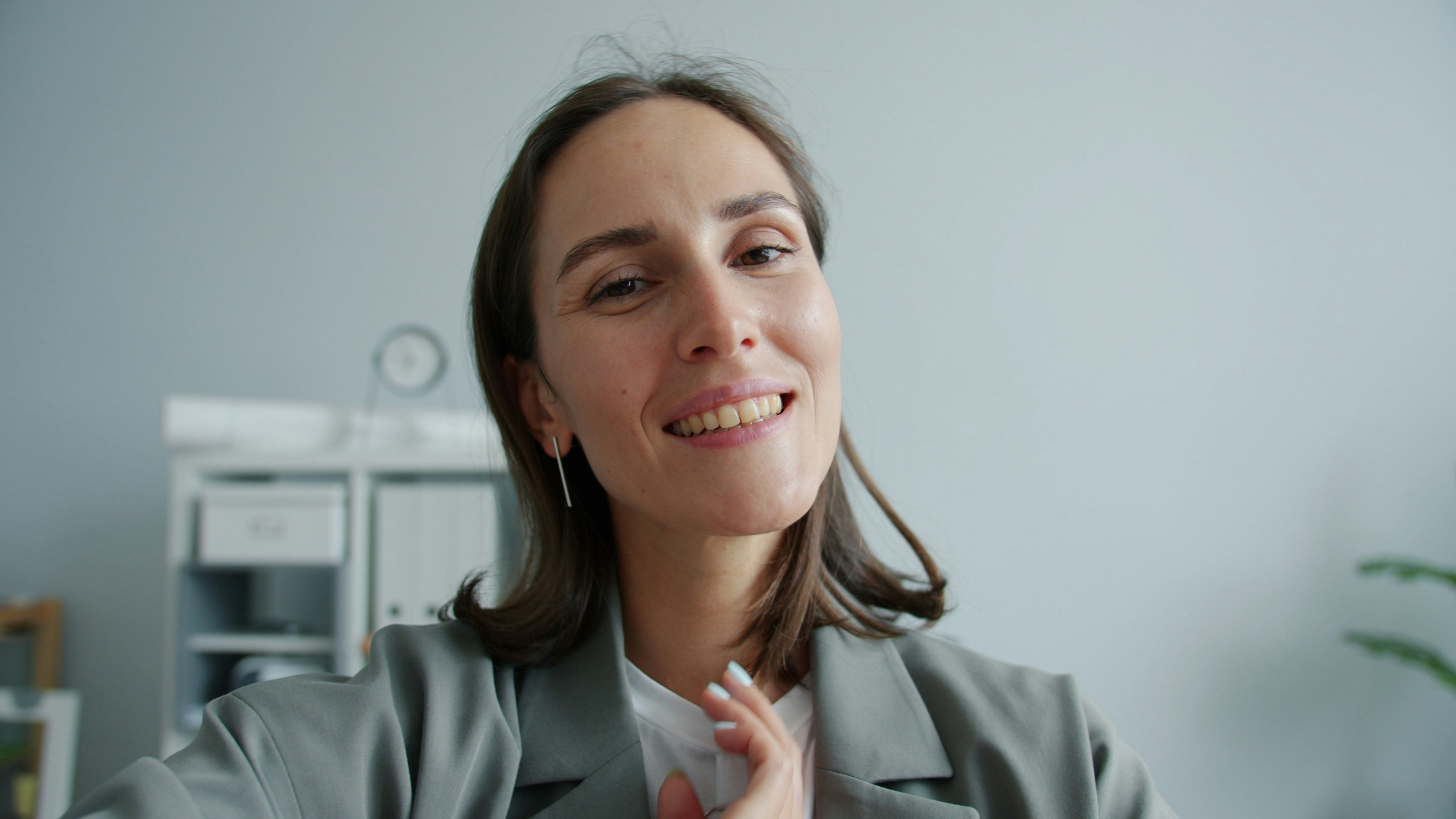 A smiling woman in a grey blazer indoors.