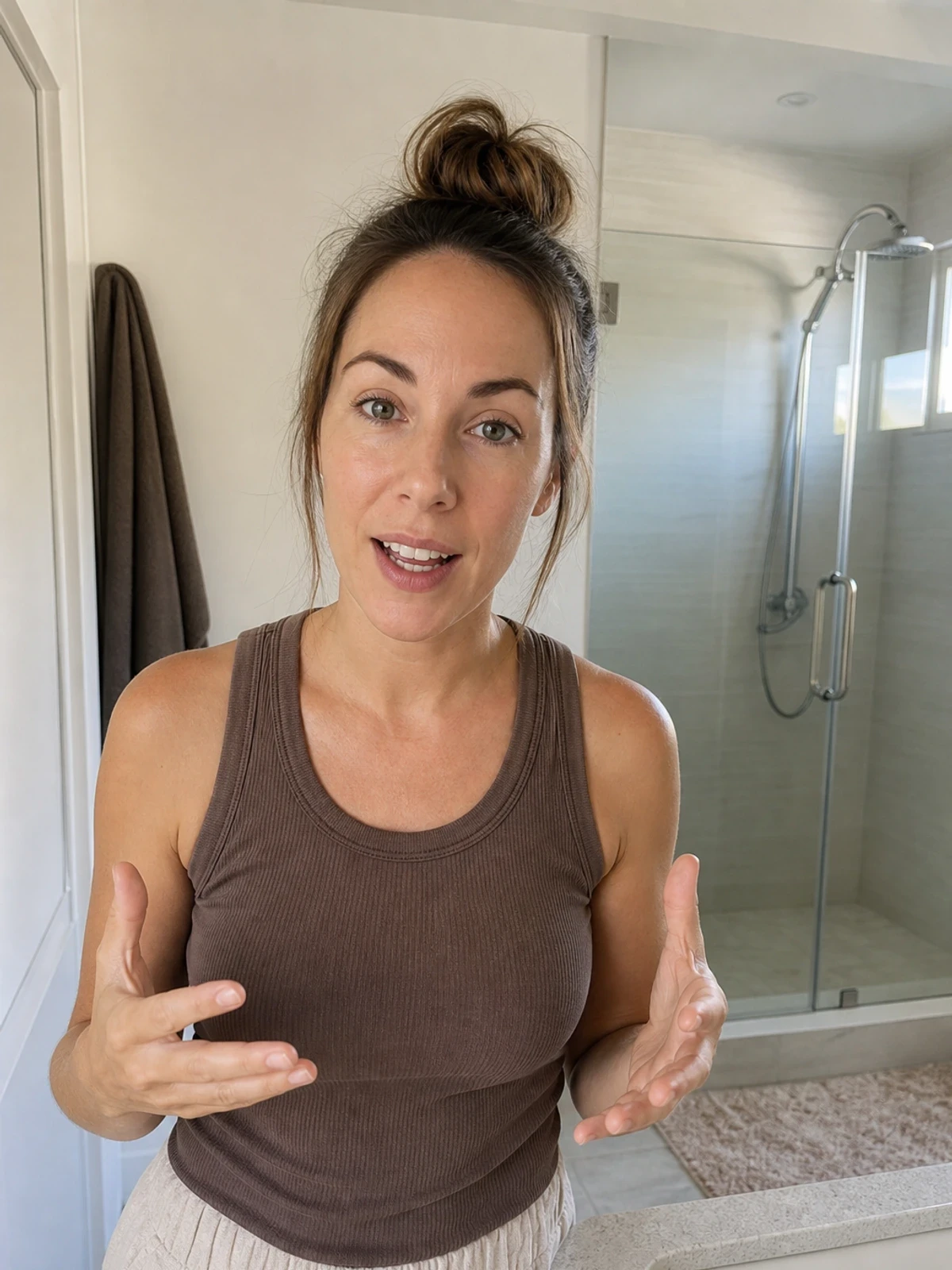 UGC-style photo: female creator in her 30s, in a bathroom mirror setup, gesturing with empty hands while talking to camera, phone-on-tripod angle.