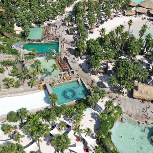 Aerial view of a water park with pools, water slides, palm trees, lounging areas, and people enjoying various attractions.