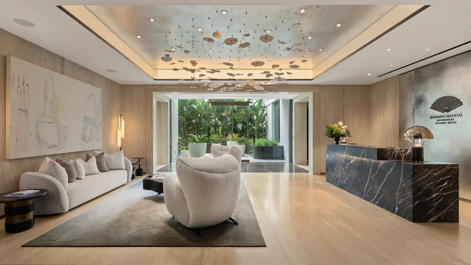 Hotel residence lobby with curved seating, a marble reception desk, and indoor greenery at the far end