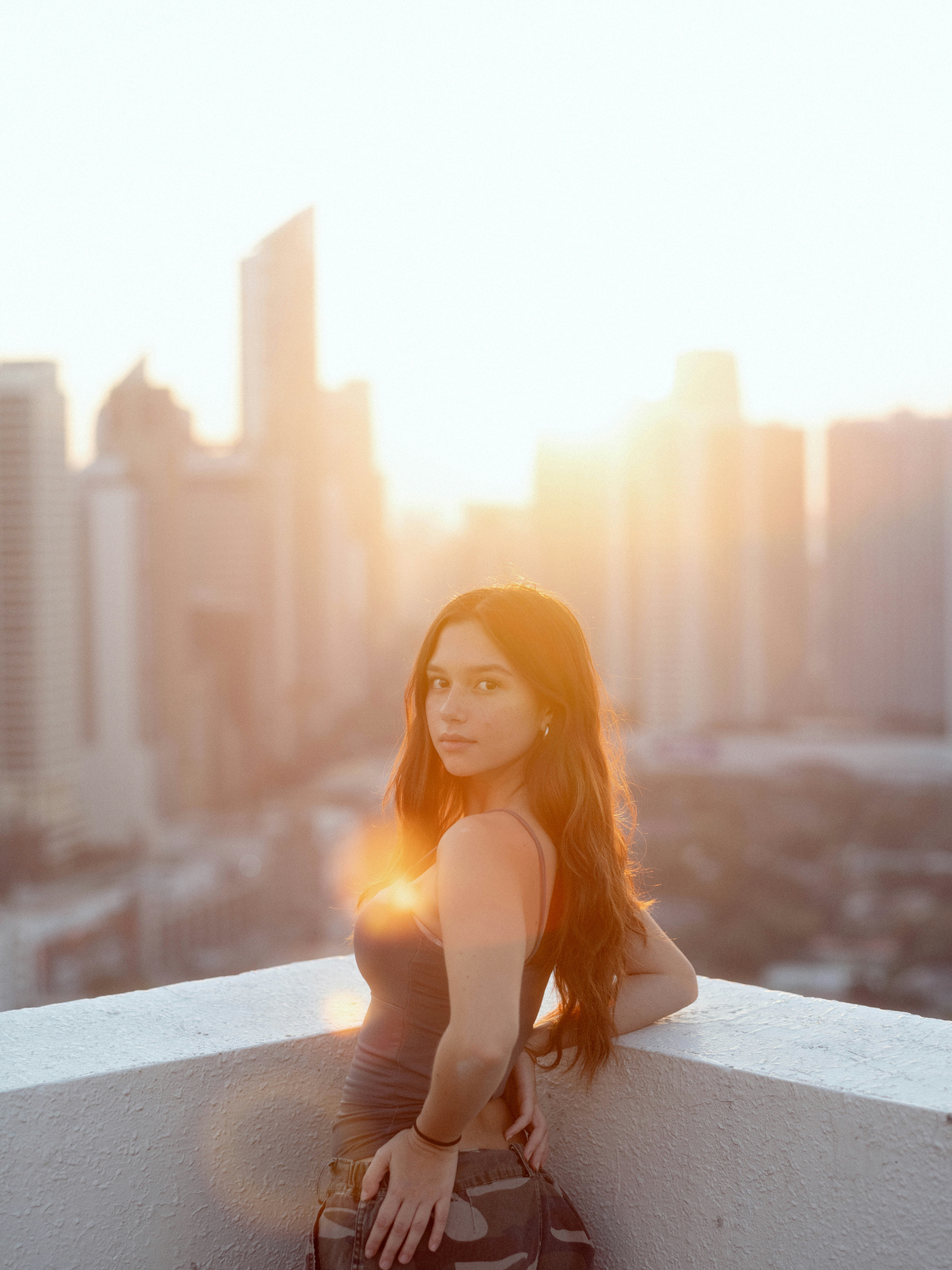 Woman posing on a rooftop with city skyline at sunset