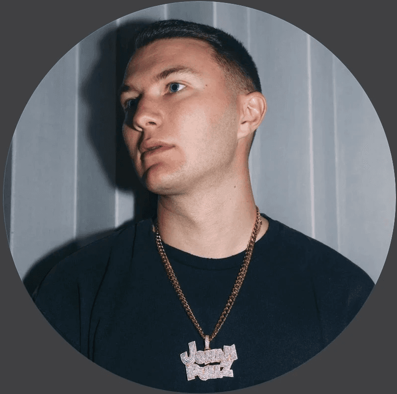 Woman in sunglasses poses against vibrant red background, wearing a beige blazer and black top. Sunlight casts dynamic shadows, creating a stylish, confident mood.