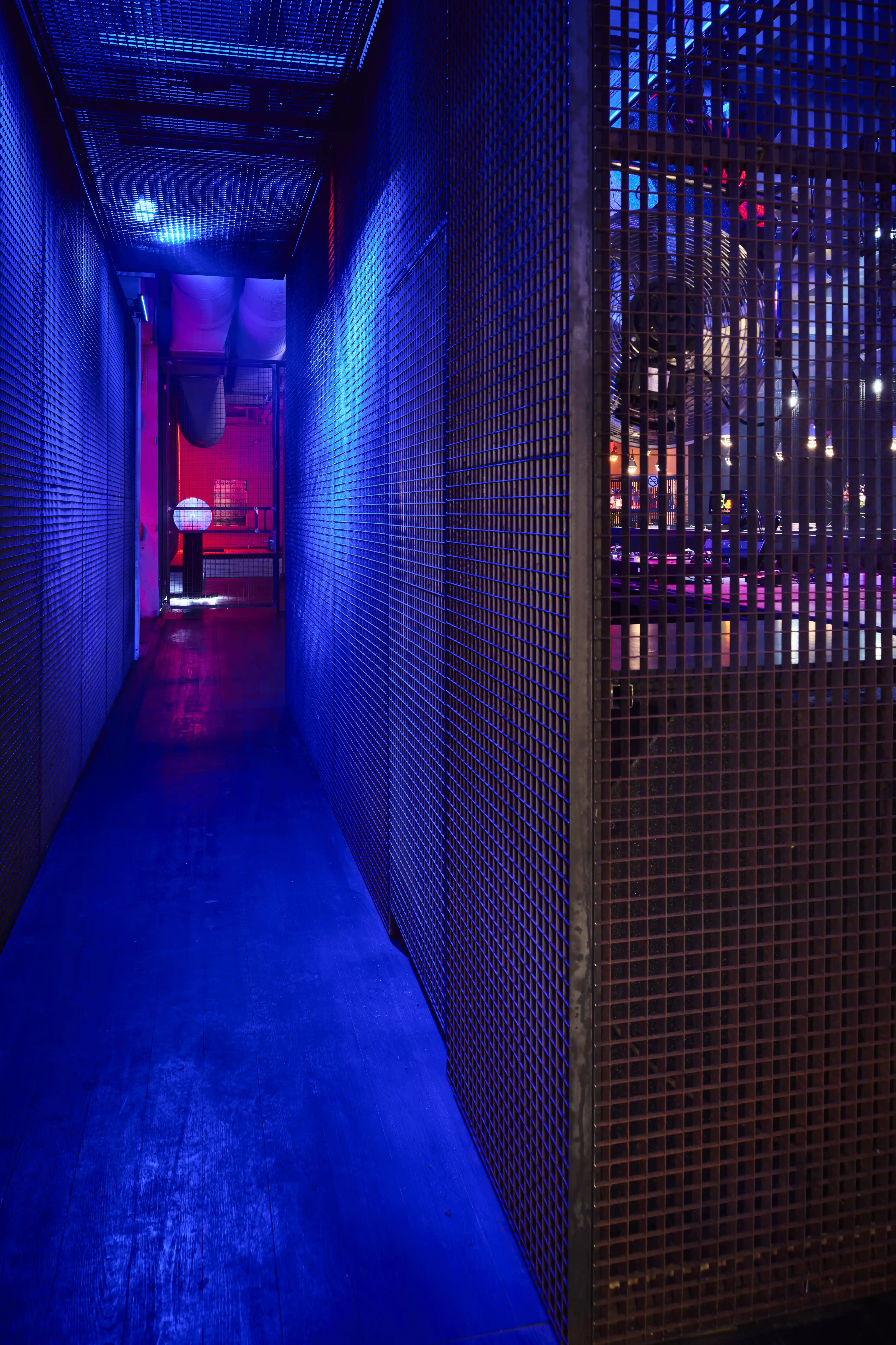 Blue-lit corridor at TRESOR GLOBUS between metal mesh walls, with a glowing floor and a pink-lit room at the far end.
