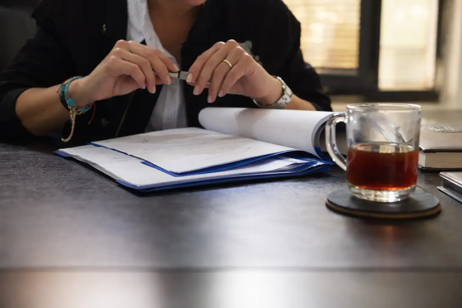 Person holding a pen over documents on a desk beside a glass of tea.