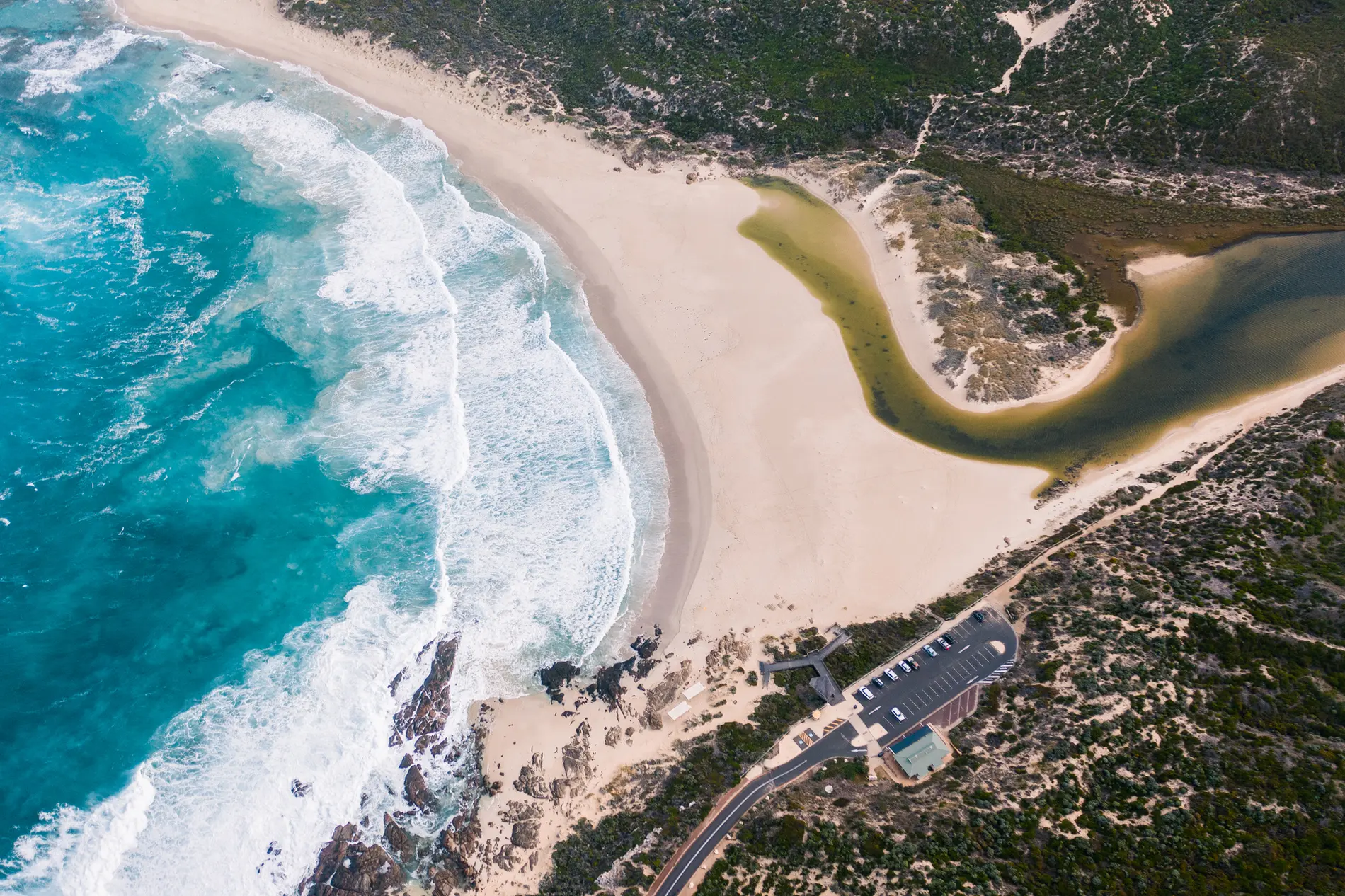 Aerial of surf breaking onto a sandy beach beside a still coastal lagoon