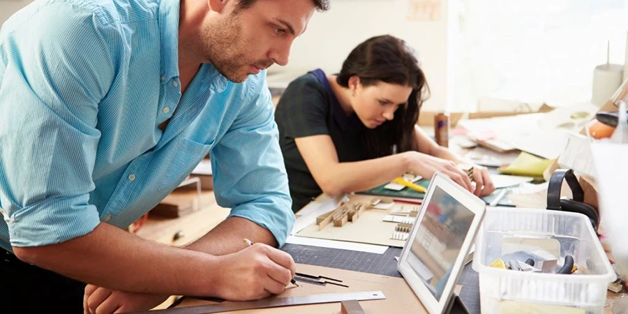 Two people working on creative design projects at a shared workspace.