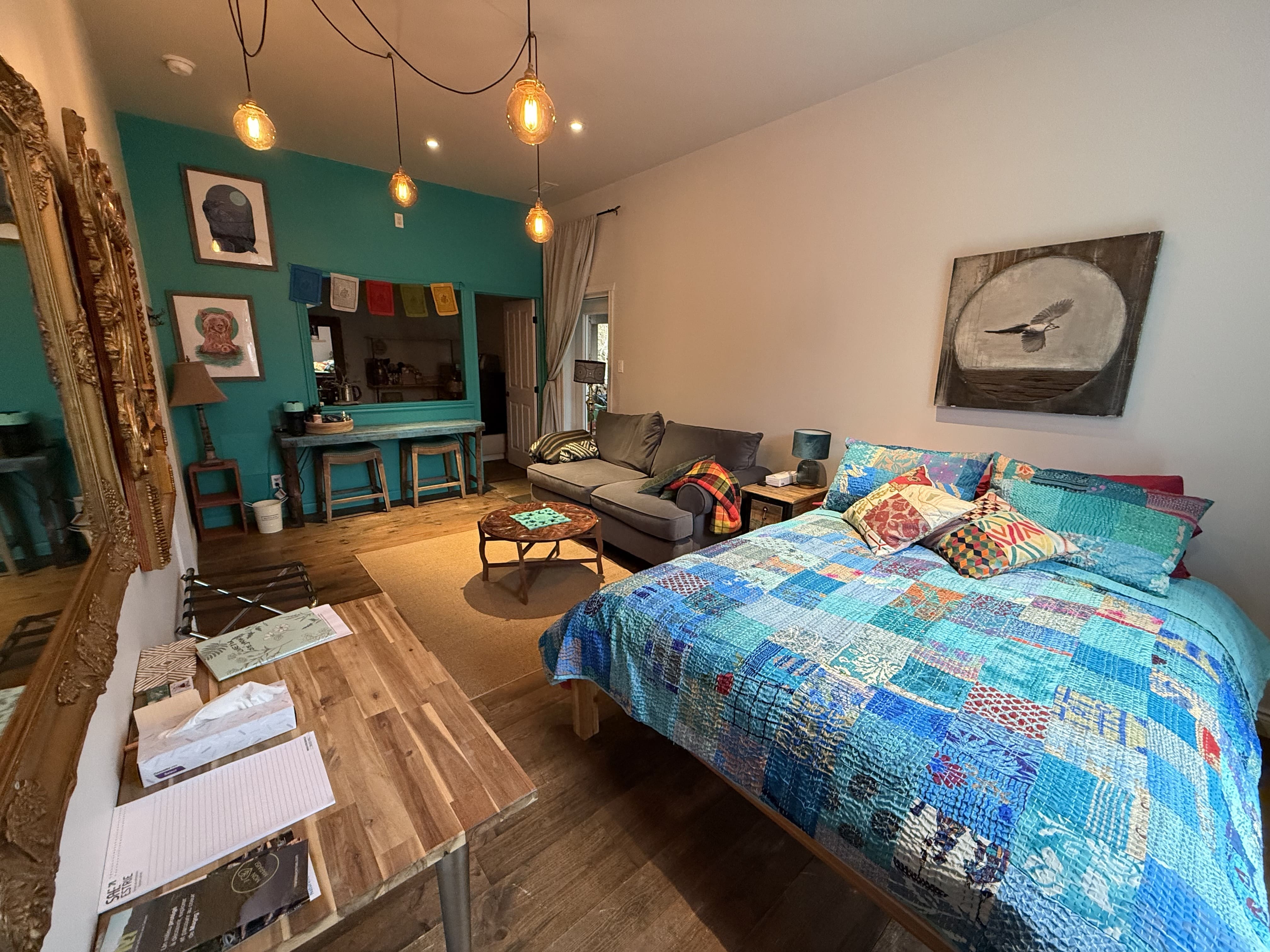 Lit et canapé gris, table basse sculptée en bois, rideaux clairs et éclairage suspendu chaleureux.