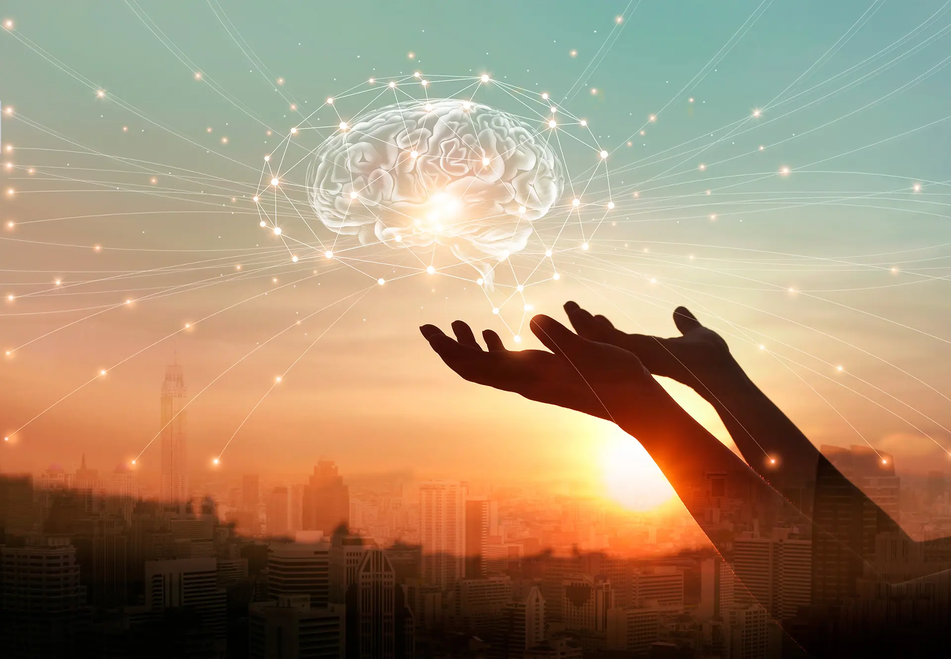 Silhouetted hands reaching toward a glowing brain with neural network connections above a city skyline at sunset, representing AI and cognitive technology