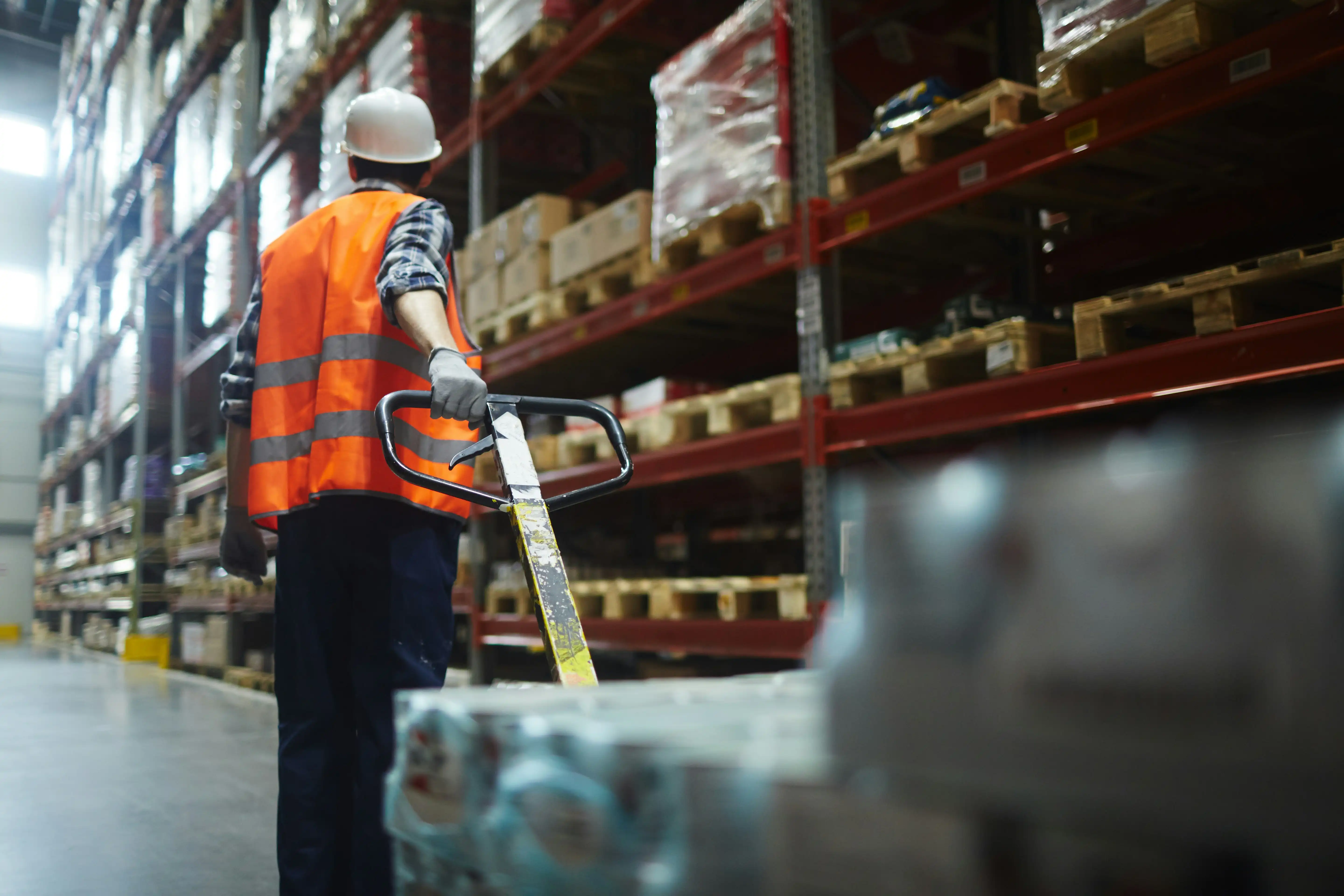warehouse worker in bright orange high-vis jacket dragging a pallet trolley