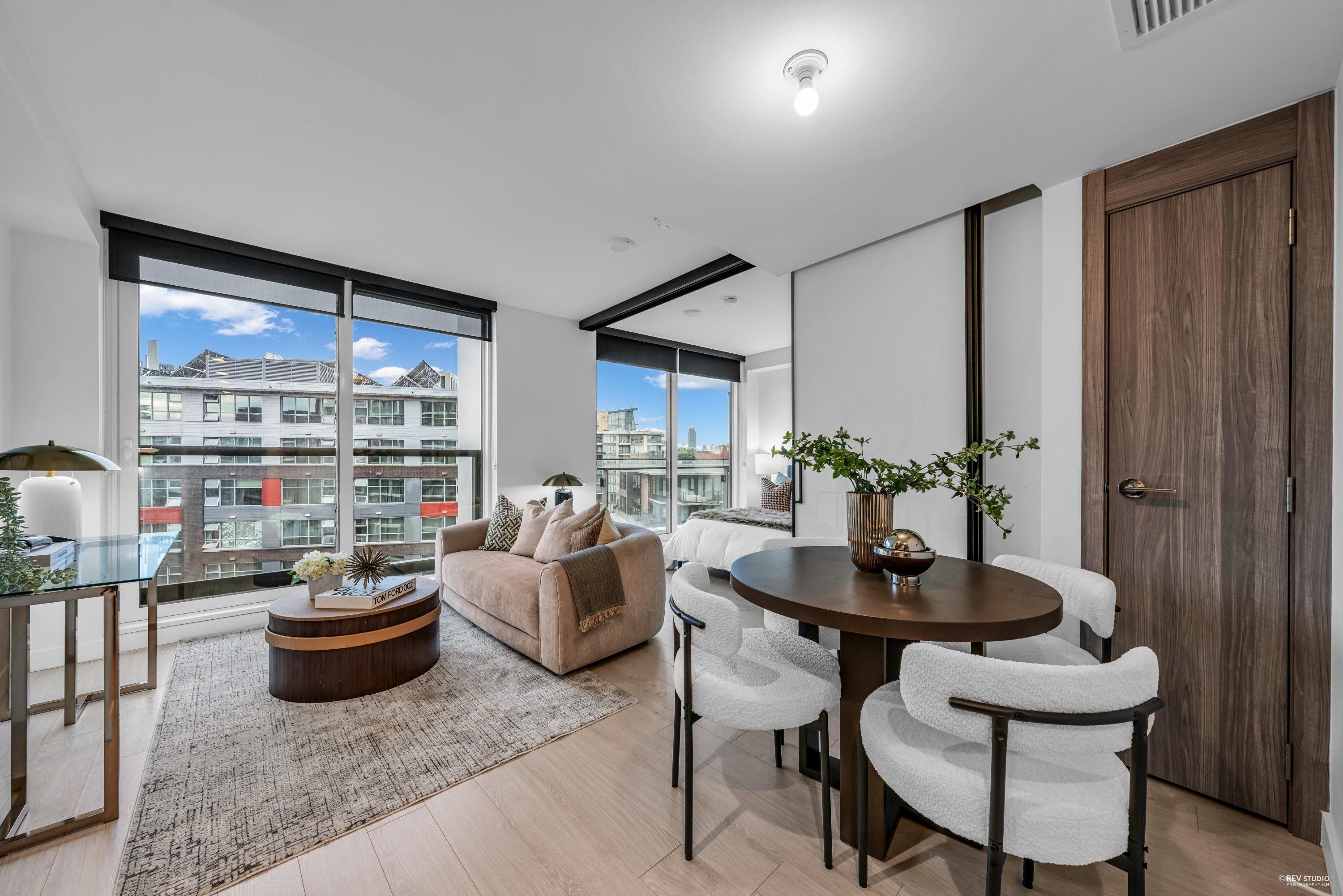 Modern living room featuring large windows, stylish furniture, and a dining area with greenery accents.
