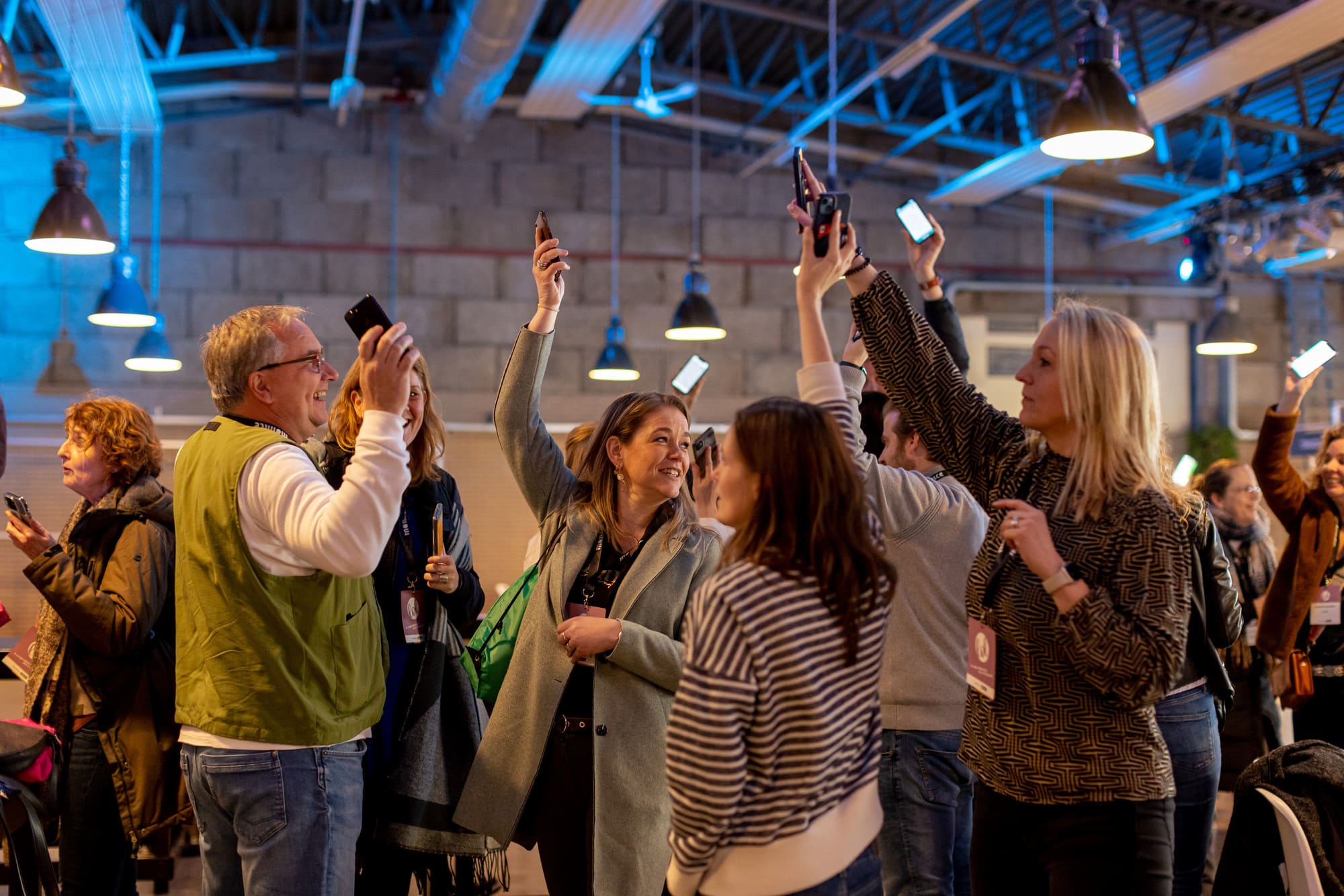 Groep mensen die samen in een zaal staan en hun smartphones omhoog houden tijdens een interactieve activiteit.