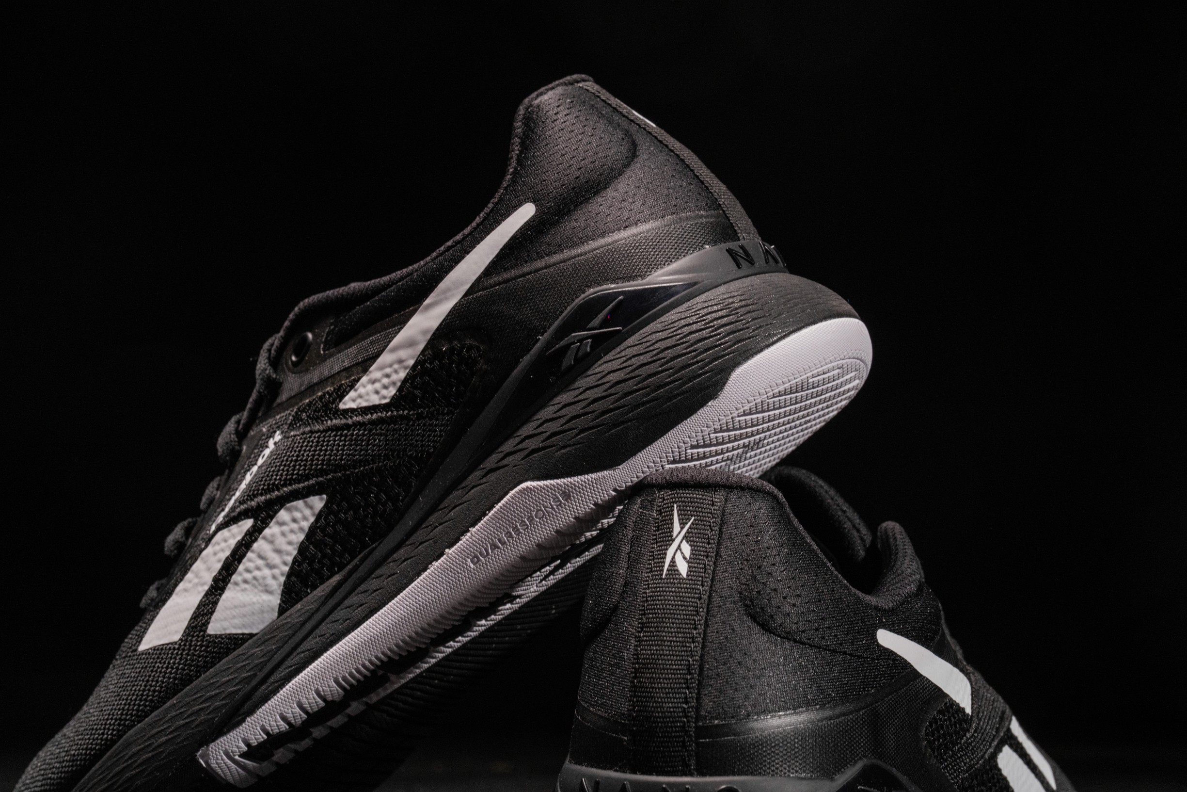 A pair of black Reebok training shoes with white accents displayed on a dark background for product photography.